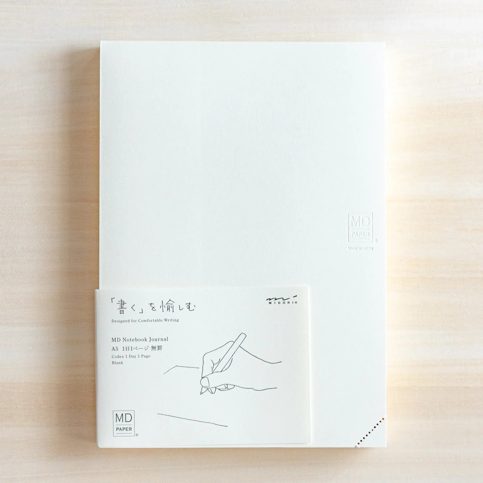 Midori Japanese journal with plain white cover and illustrated paper band showing hand drawing on light wood.