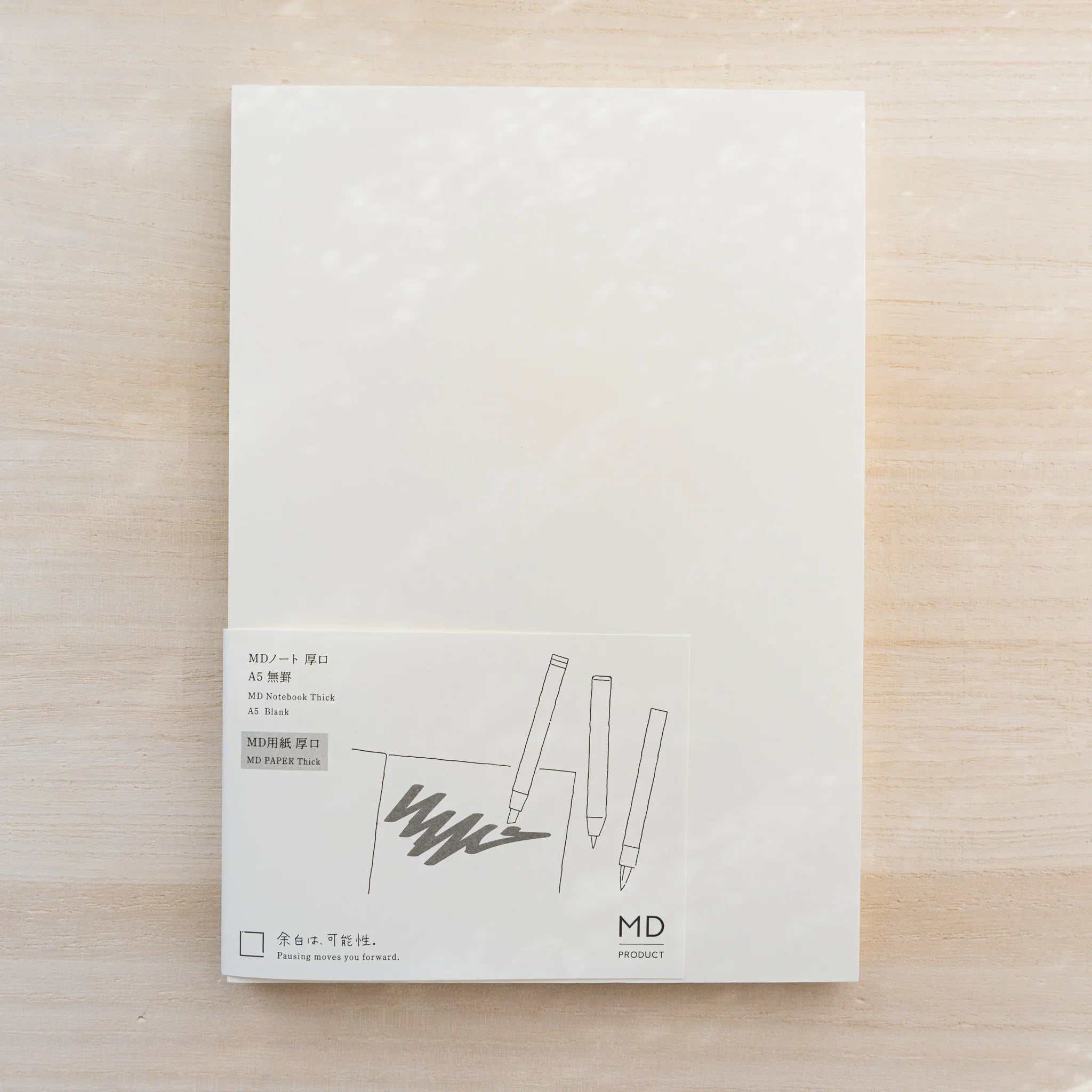Midori MD Notebook Thick white cover with paper belly band reading MD Notebook Thick A5 Blank and three-pens line drawing