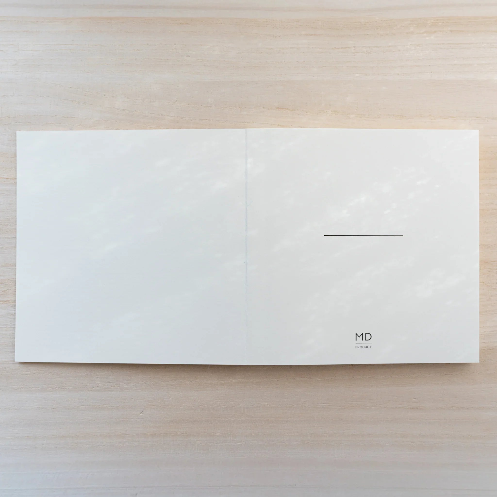 MD Notebook Thick Paper A5 Square opened flat, blank cream square spread with small MD logo and line