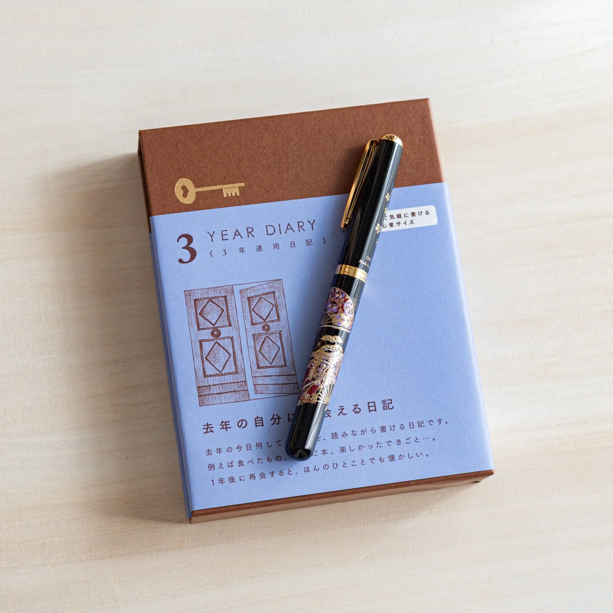 Japanese journal Midori 3-year diary blue-brown box with gate design, decorative black pen placed diagonally.
