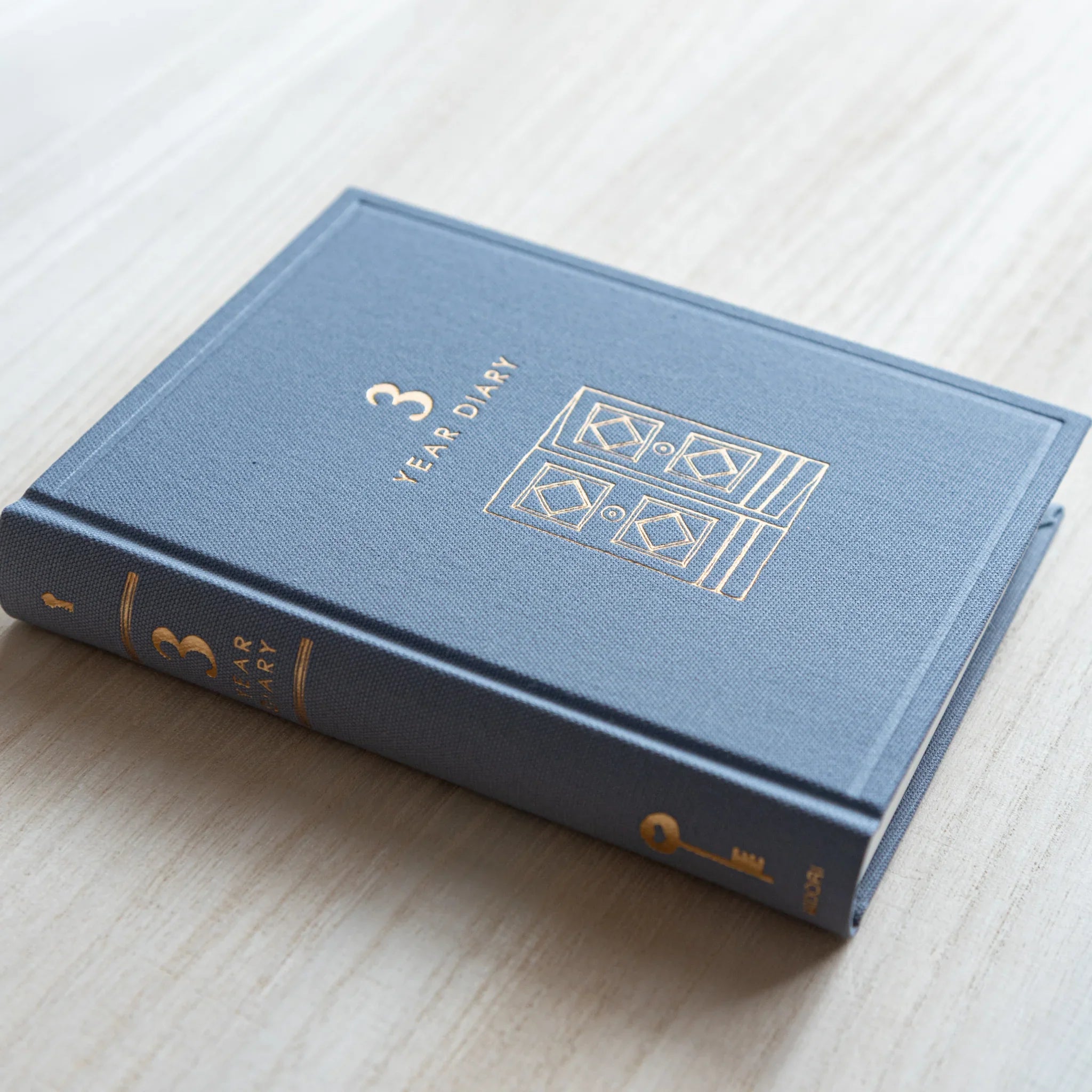 Japanese journal Midori 3-year diary closed gray cover with gold gate motif and spine, angled side view on table