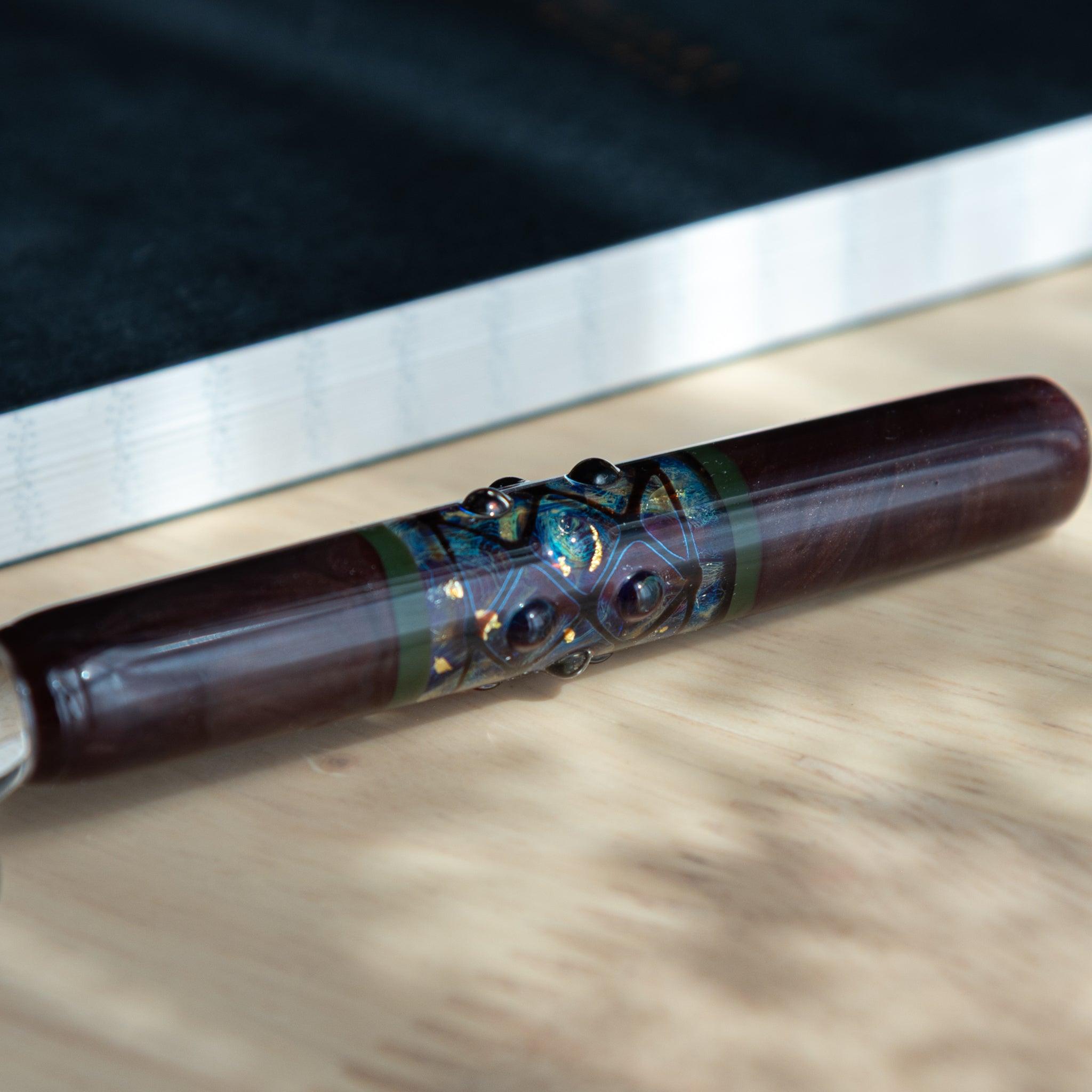 Close-up of a maroon glass dip pen from Japan, featuring an ornate central band with raised patterns and iridescent colors.