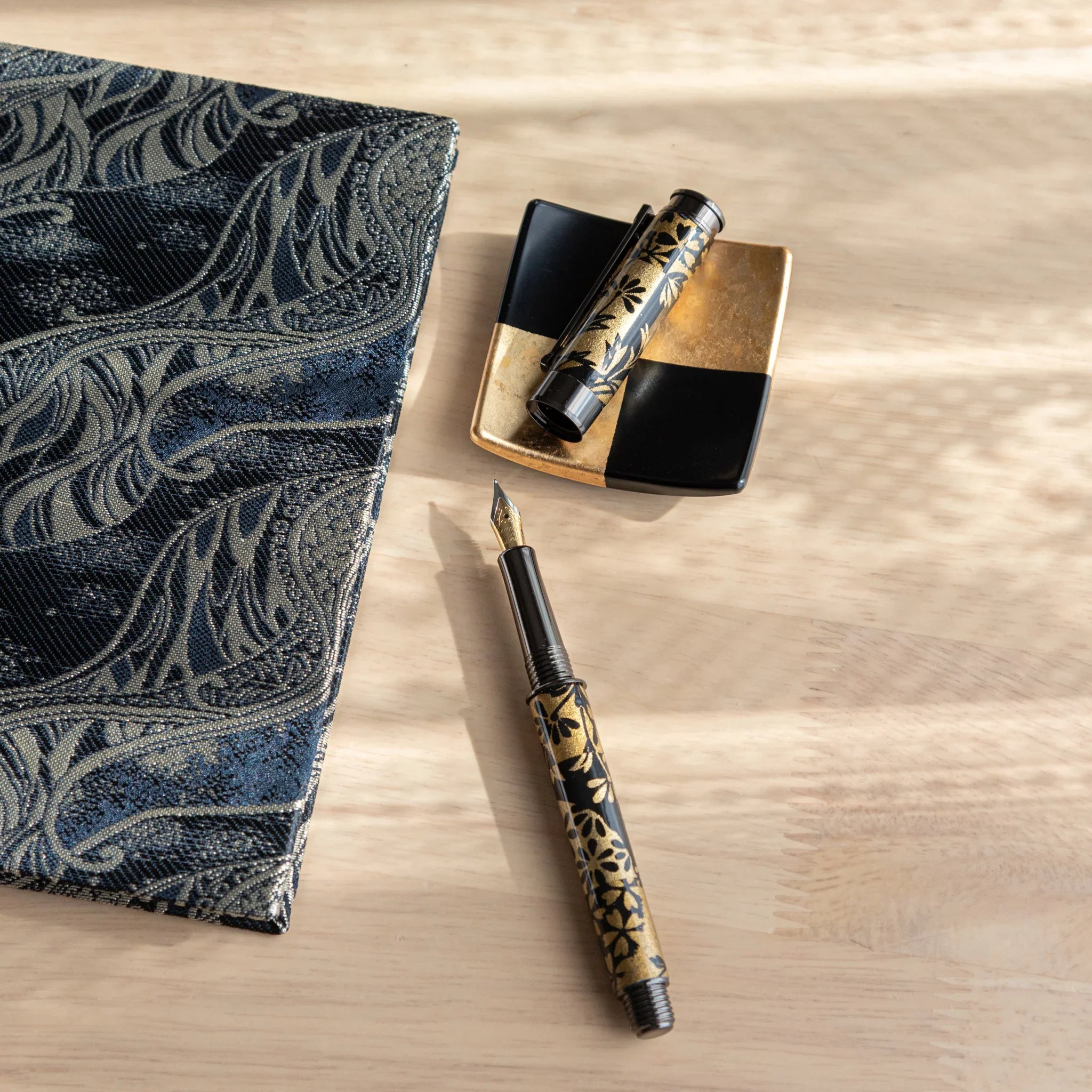 Black fountain pen with gold and navy botanical pattern displayed on autumn grasses Mino washi fabric background