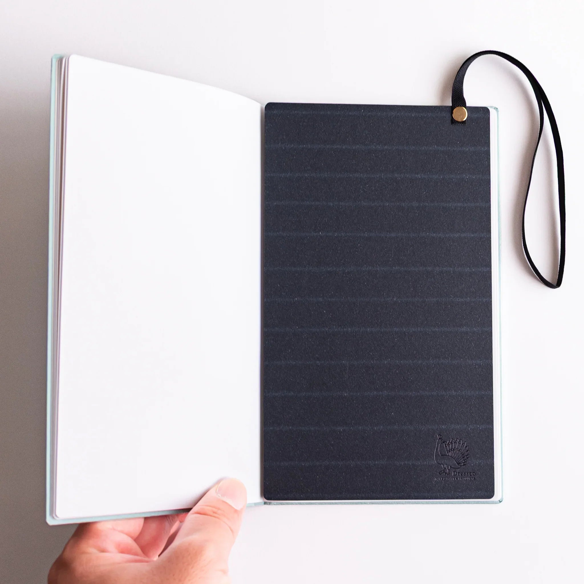 Navy band with strap and clasp in open notebook; Dressco B6 accessory serving as closure, bookmark and writing board.
