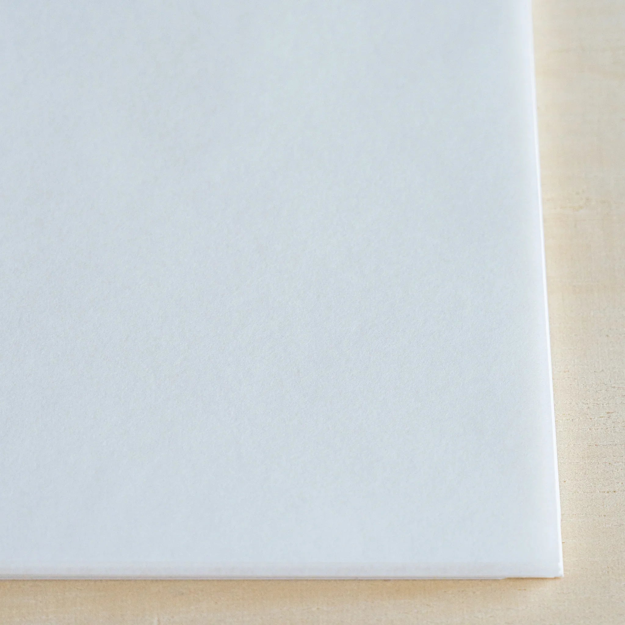 Close-up of MVP Onion Skin paper corner on light wood, showing the smooth white surface and thin sheet edge