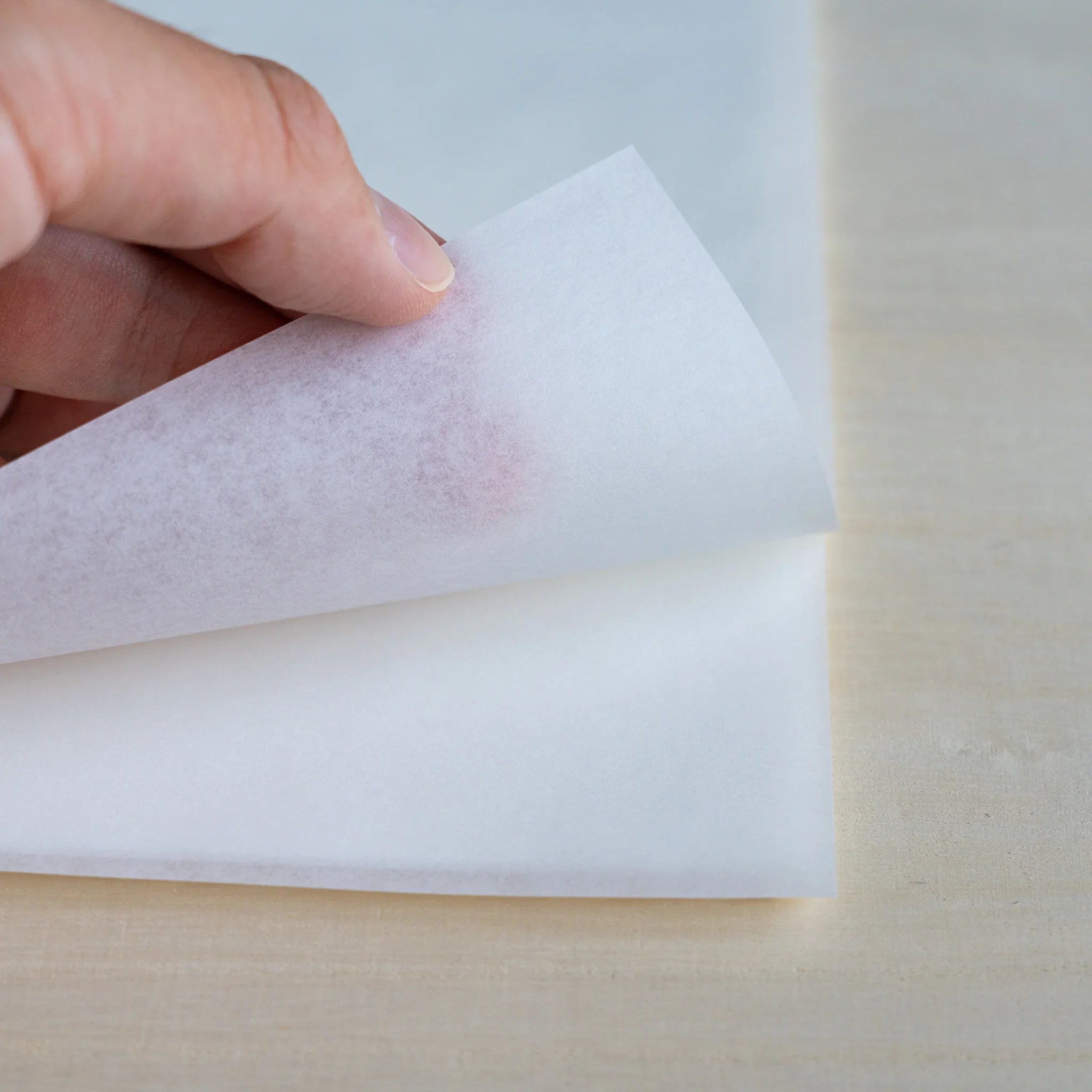 Hand lifting a sheet of MVP Onion Skin paper, faint reddish ink from the other side visible through the thin paper