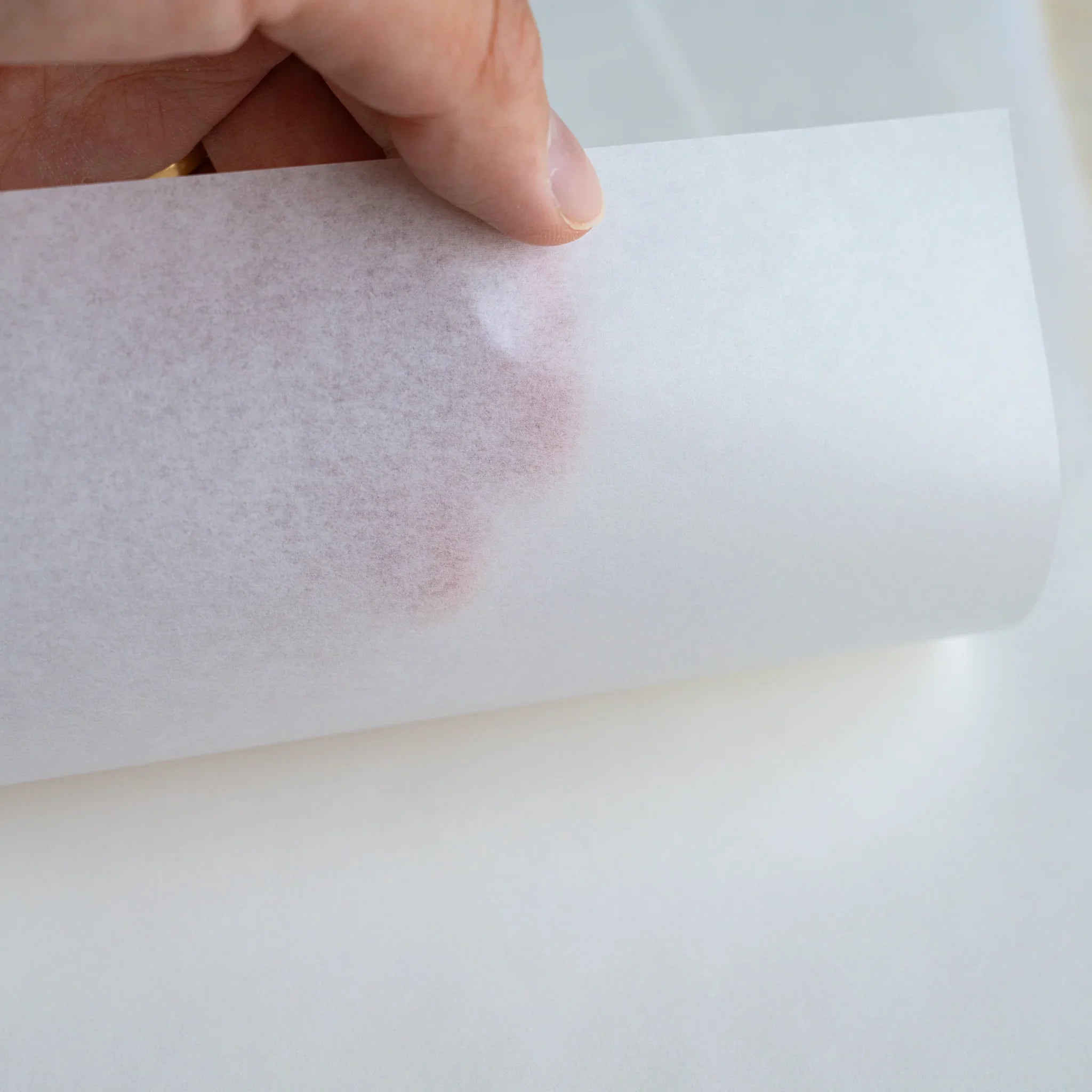 Close-up of MVP Onion Skin paper held by hand, reddish brown ink mark from the reverse side visible through the sheet