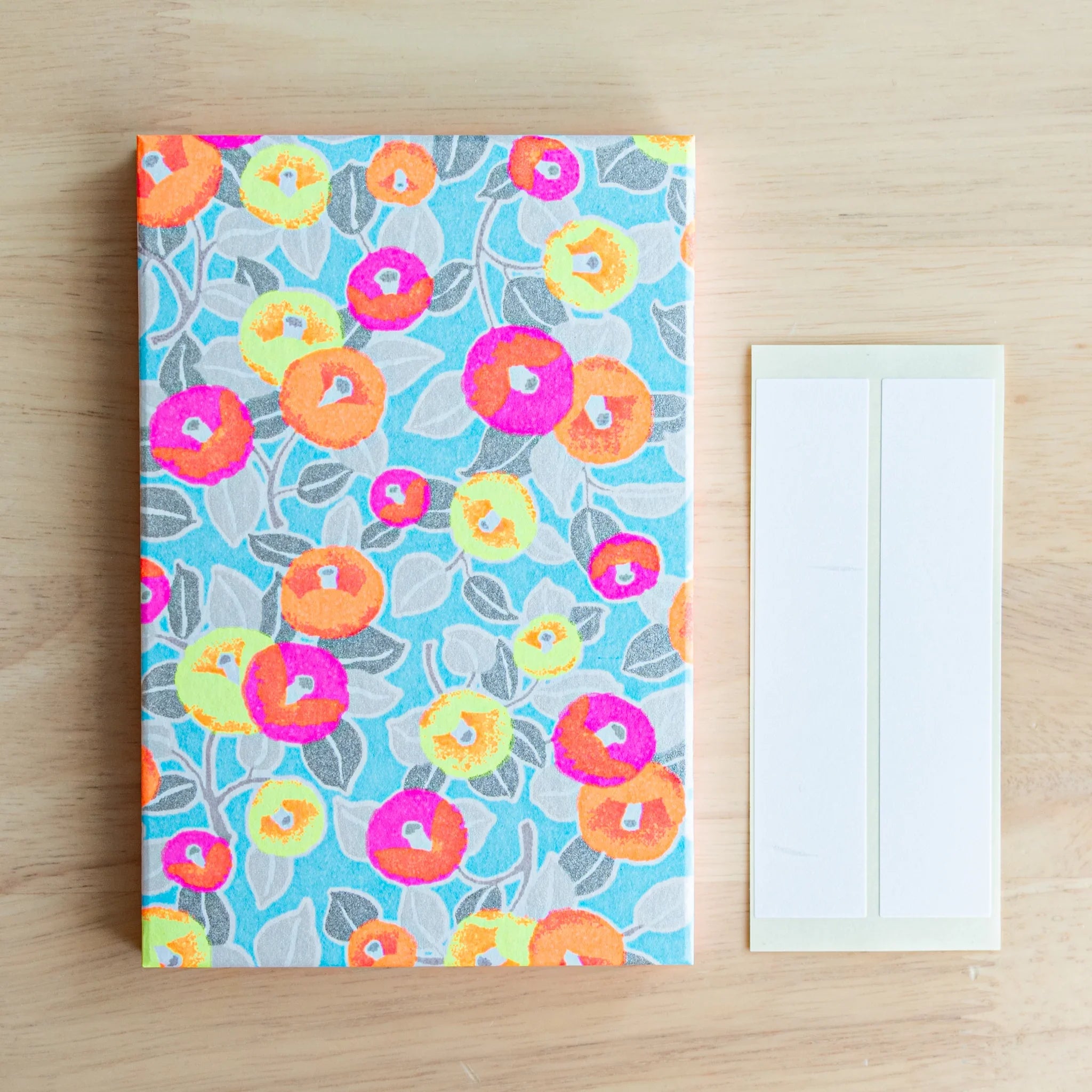 Neon Camellia washi goshuincho front cover flat lay on wood surface beside two included cream washi name label strips