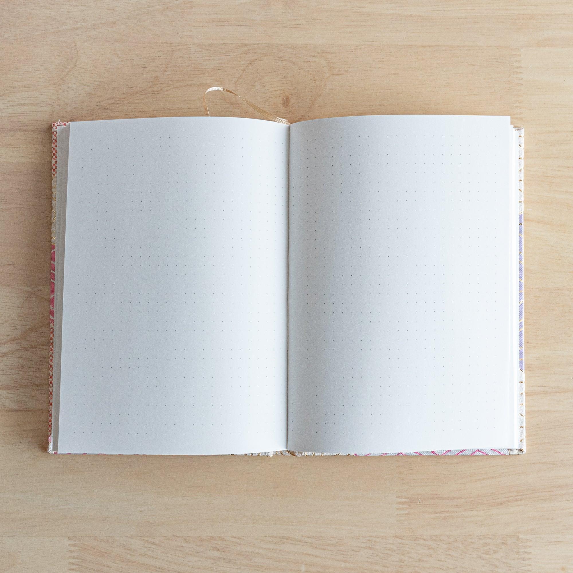 An open Japanese notebook showing white pages with a subtle dot grid pattern, ideal for writing or sketching.