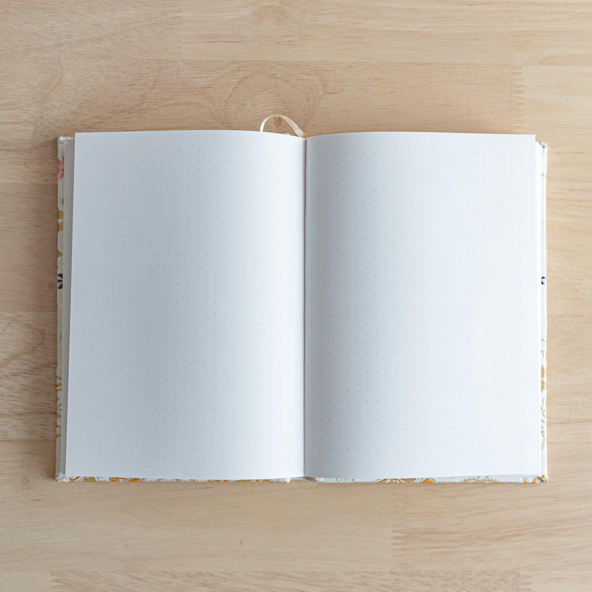 An open Japanese notebook showing white pages with a subtle dot grid pattern, ideal for writing or sketching.