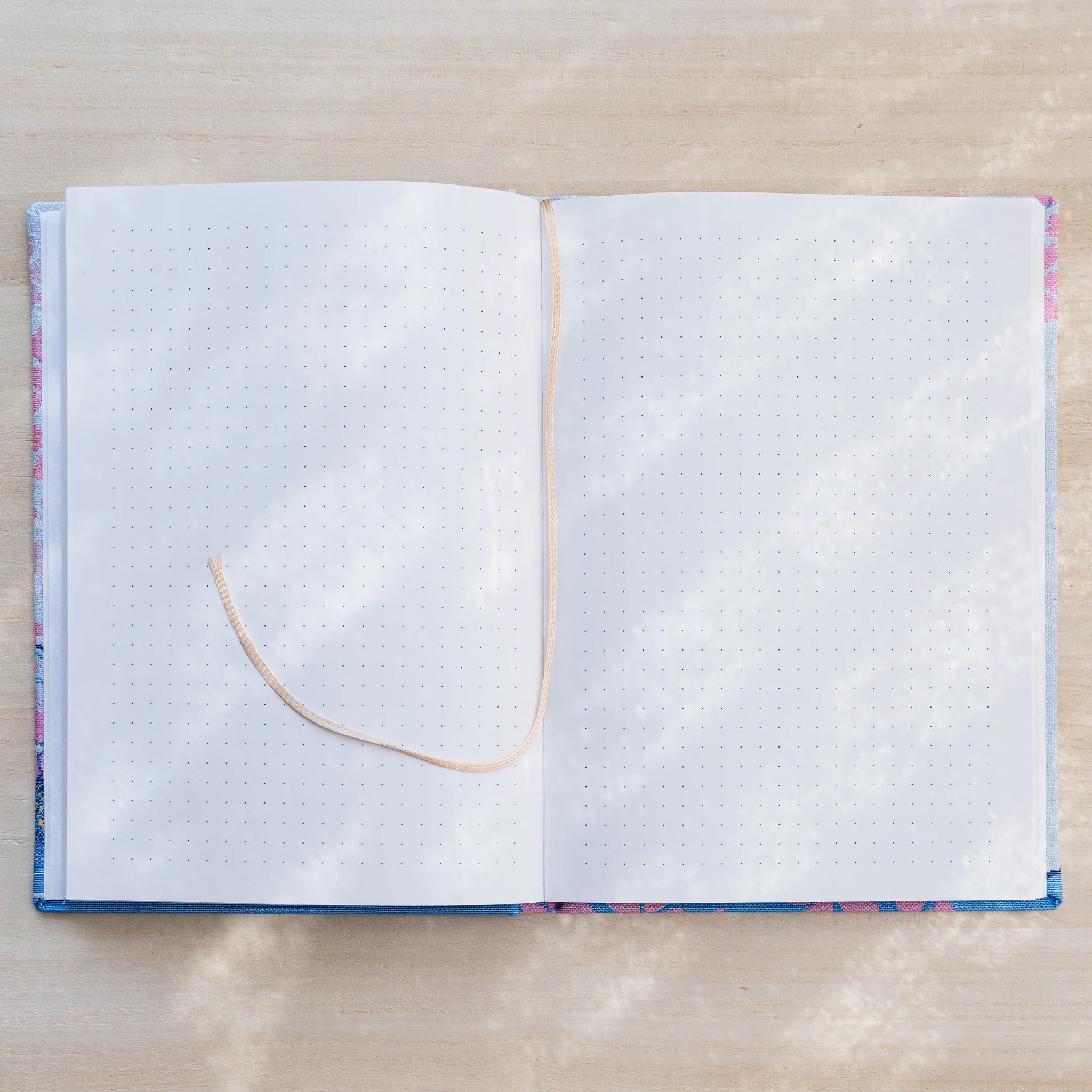 Notebook open flat to dot grid pages on both sides with a beige ribbon bookmark, textile cover edges visible