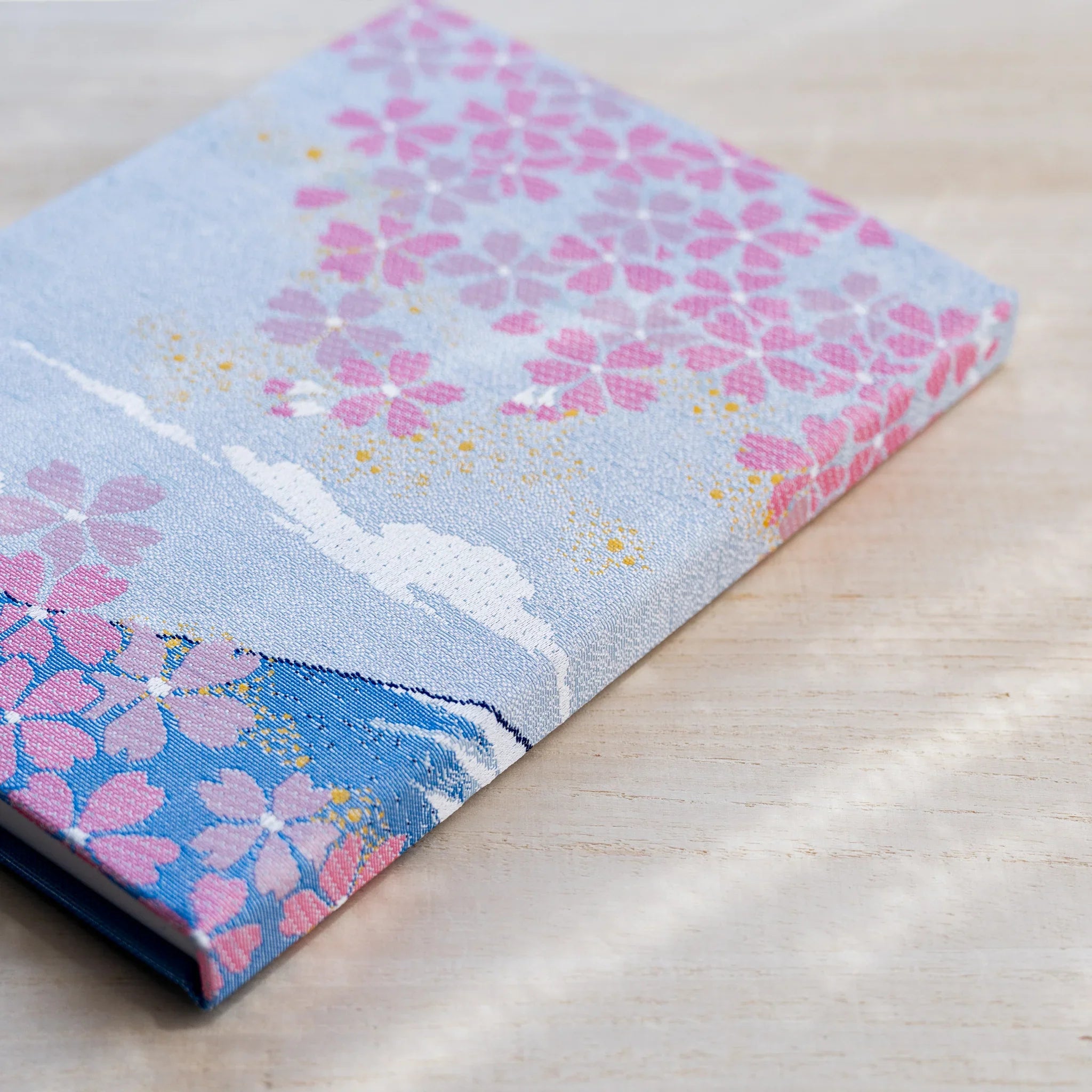 Angled view of notebook spine and cover edge in woven textile with pink cherry blossoms and blue section