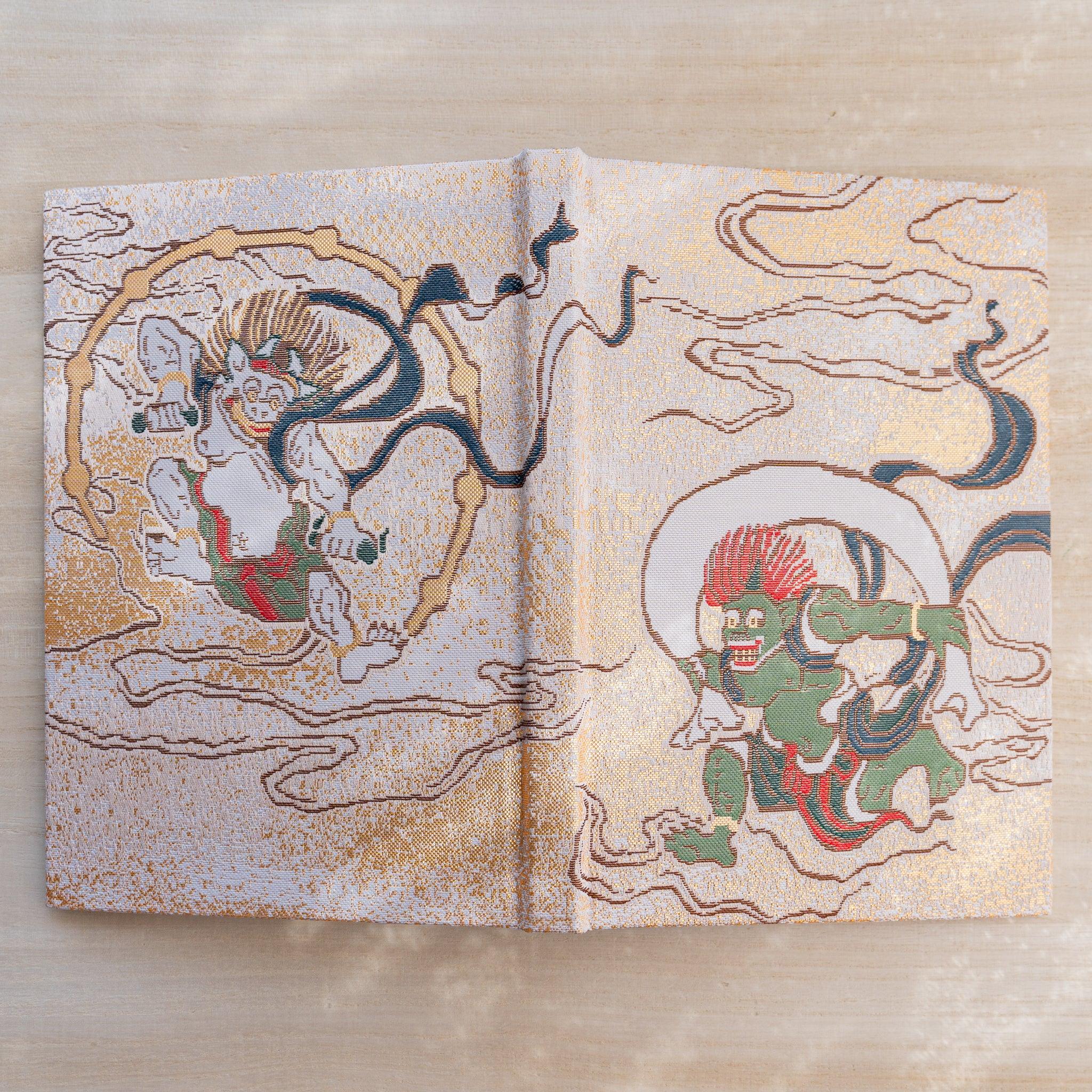 Notebook cover opened flat, woven textile with green wind god Fujin and pale thunder god Raijin on gold ground