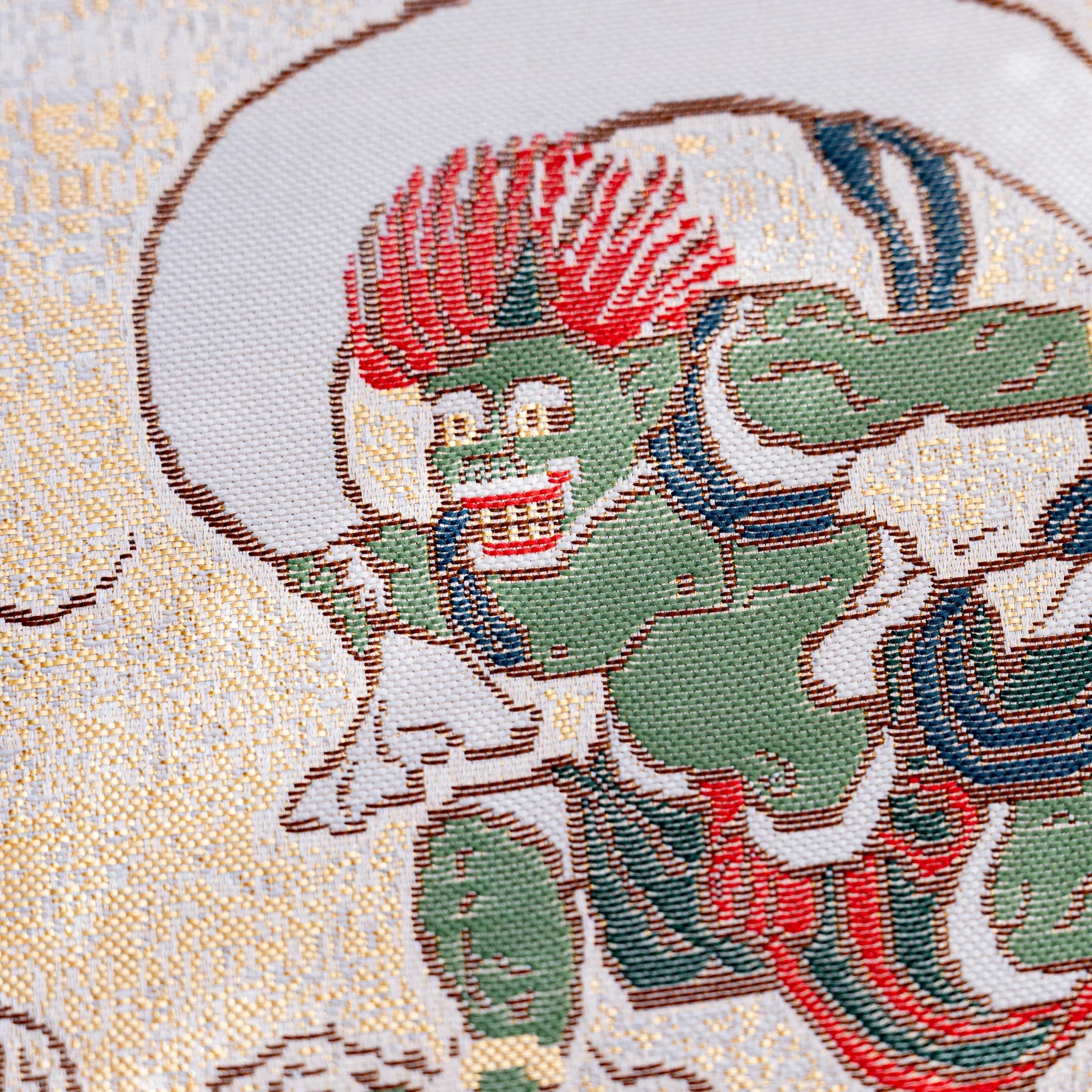 Close-up of woven textile showing green wind god Fujin with red hair and a dark wind bag