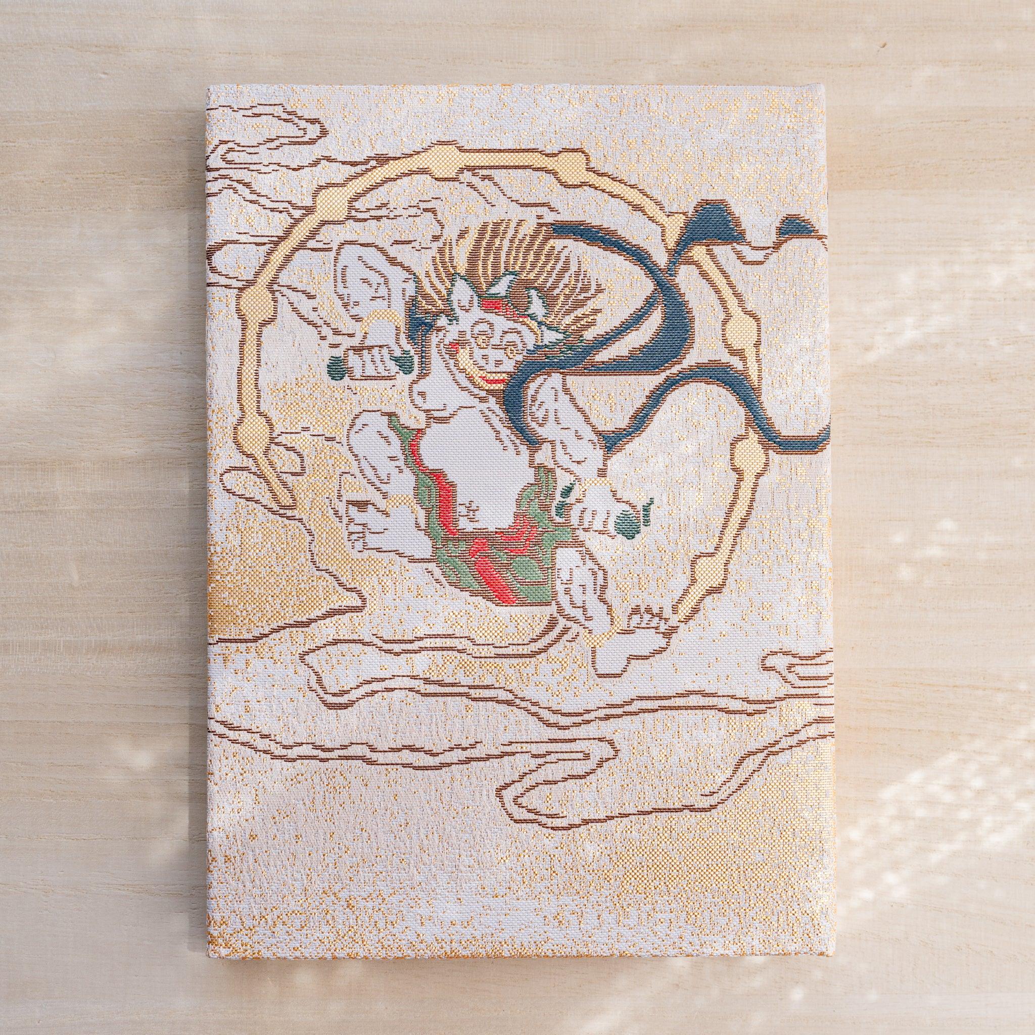 Notebook back cover in woven textile, pale thunder god Raijin encircled by drums on a gold cloud ground