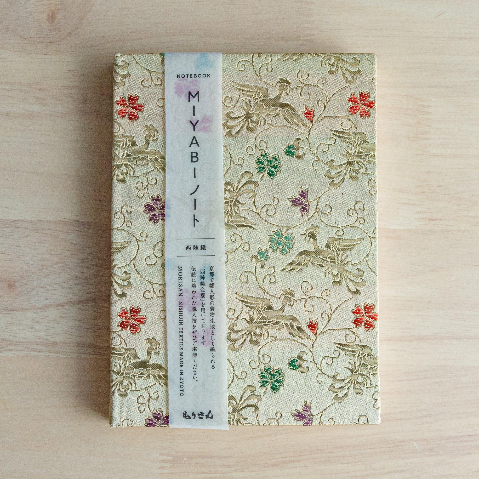 A Japanese notebook with an elegant gold fabric cover featuring intricate bird and floral patterns in red, green, and purple accents.