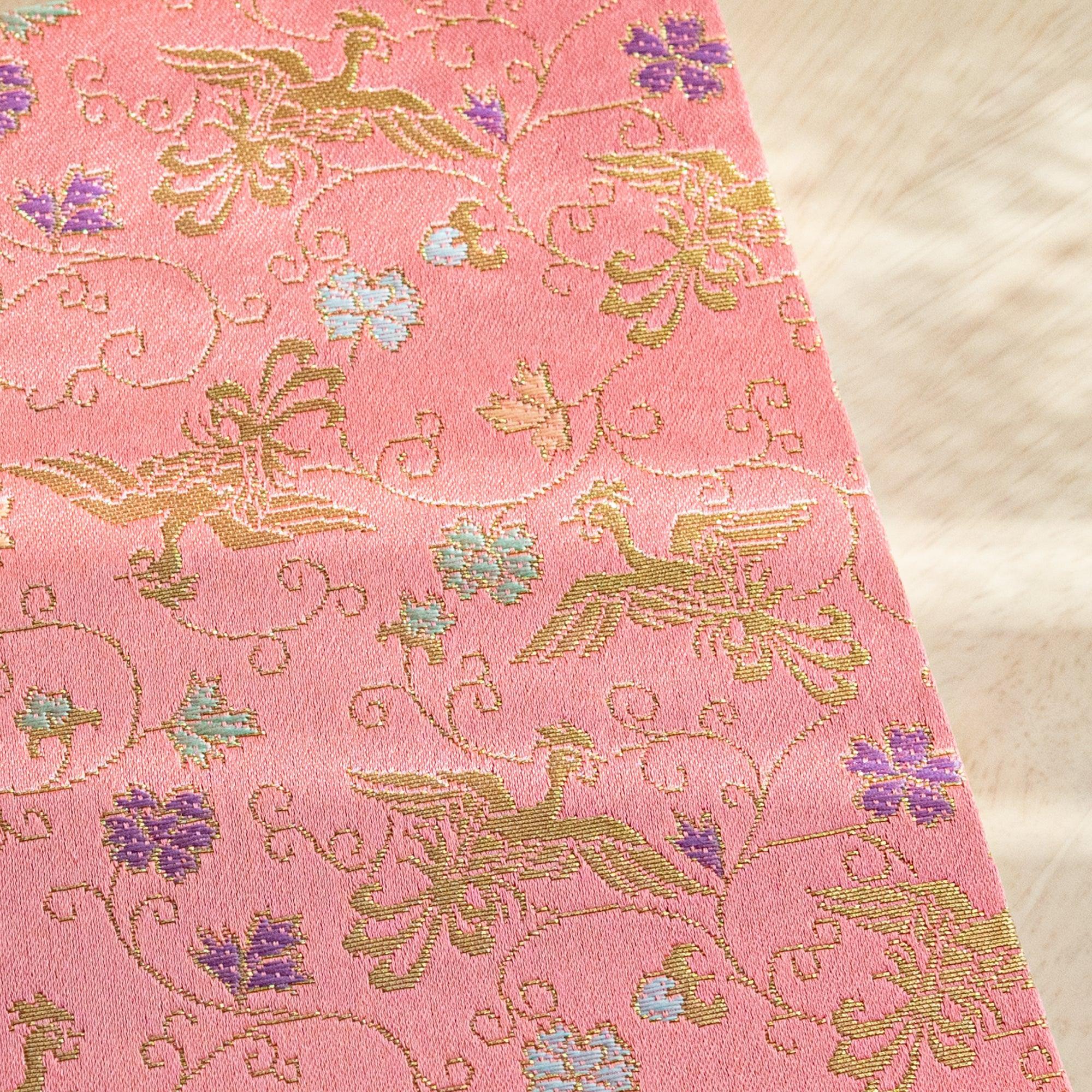 Corner close-up of pink Nishijin woven textile notebook showing gold phoenix, arabesque scrollwork and purple flower motifs
