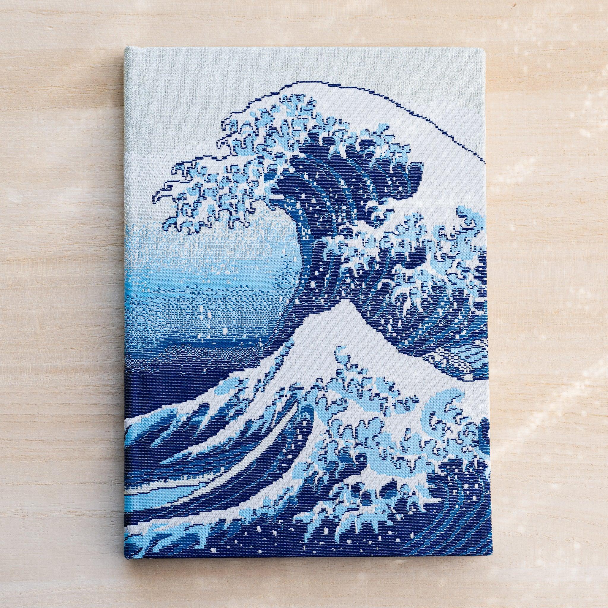 Notebook front cover in woven Nishijin textile showing the Great Wave, a large cresting blue and white wave on pale ground
