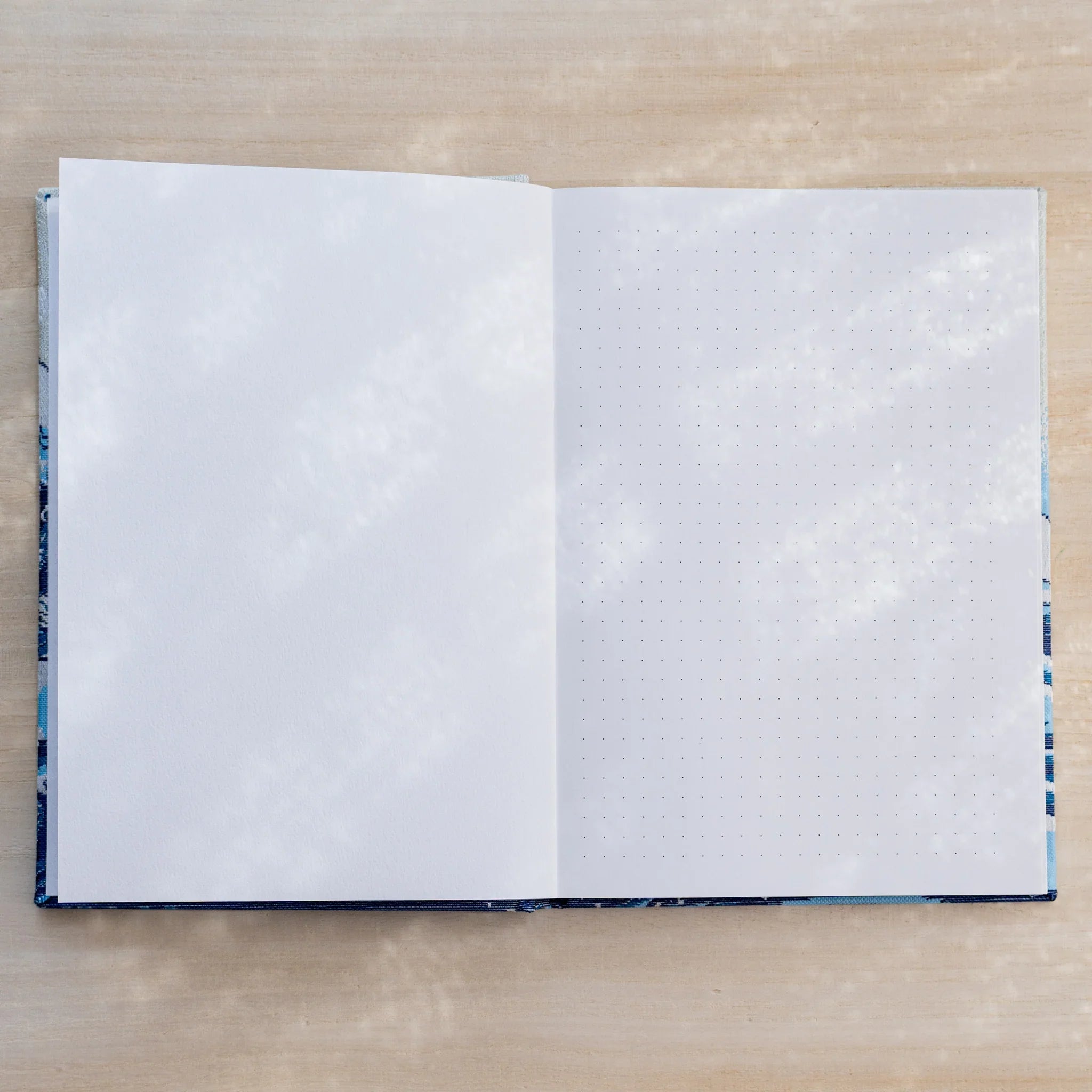 Notebook open showing a blank white page on left and a dot grid page on right, blue textile cover edges