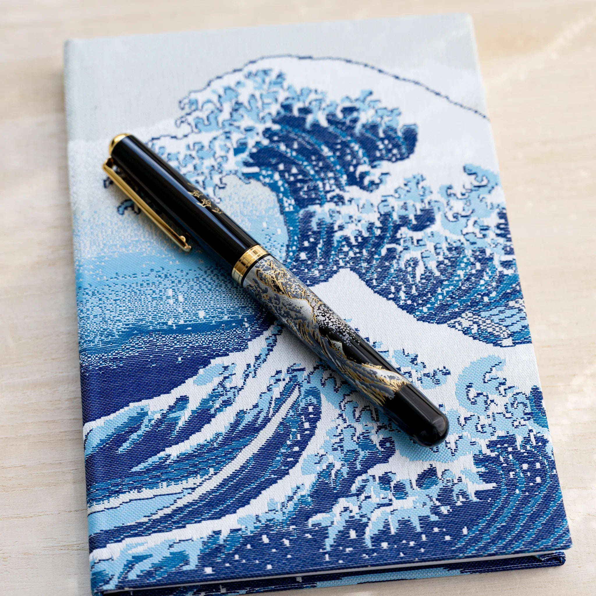 Notebook front cover with the Great Wave in blue and white woven textile, black fountain pen resting on top
