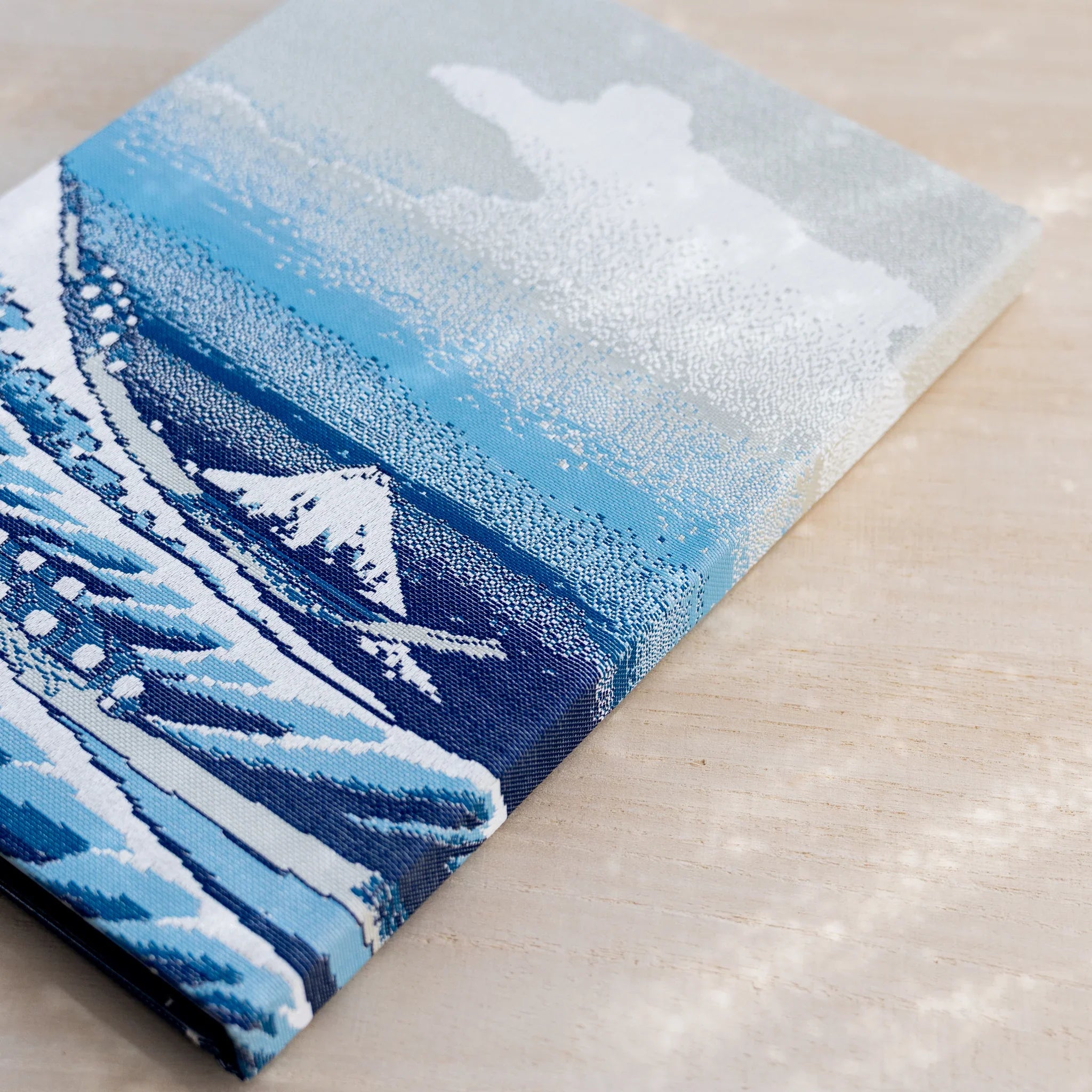 Angled view of notebook back cover in woven textile with blue waves, a white peak, and pale cloudy sky