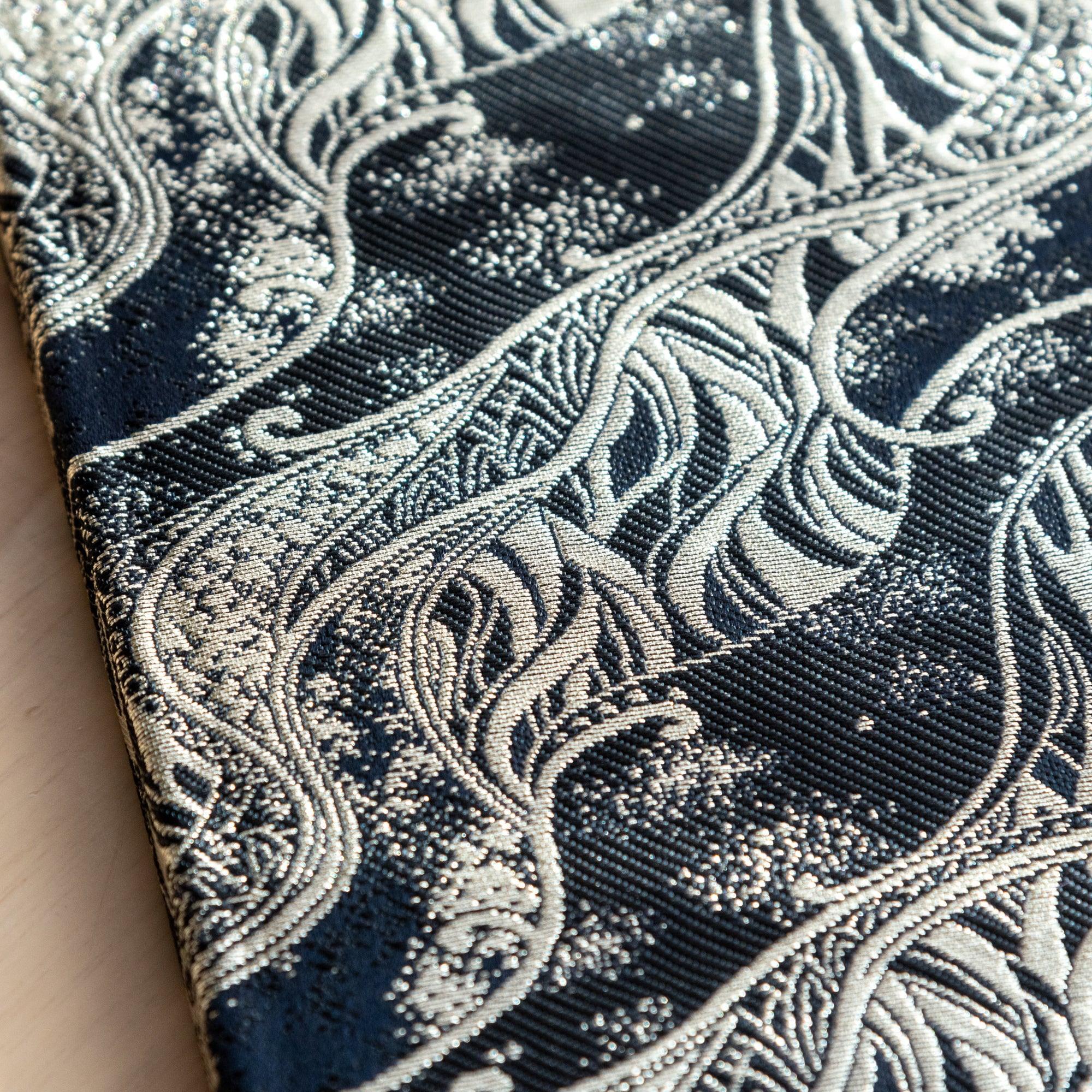 A Japanese notebook with an elegant black fabric cover featuring intricate silver wave-like patterns, placed on a wooden table.