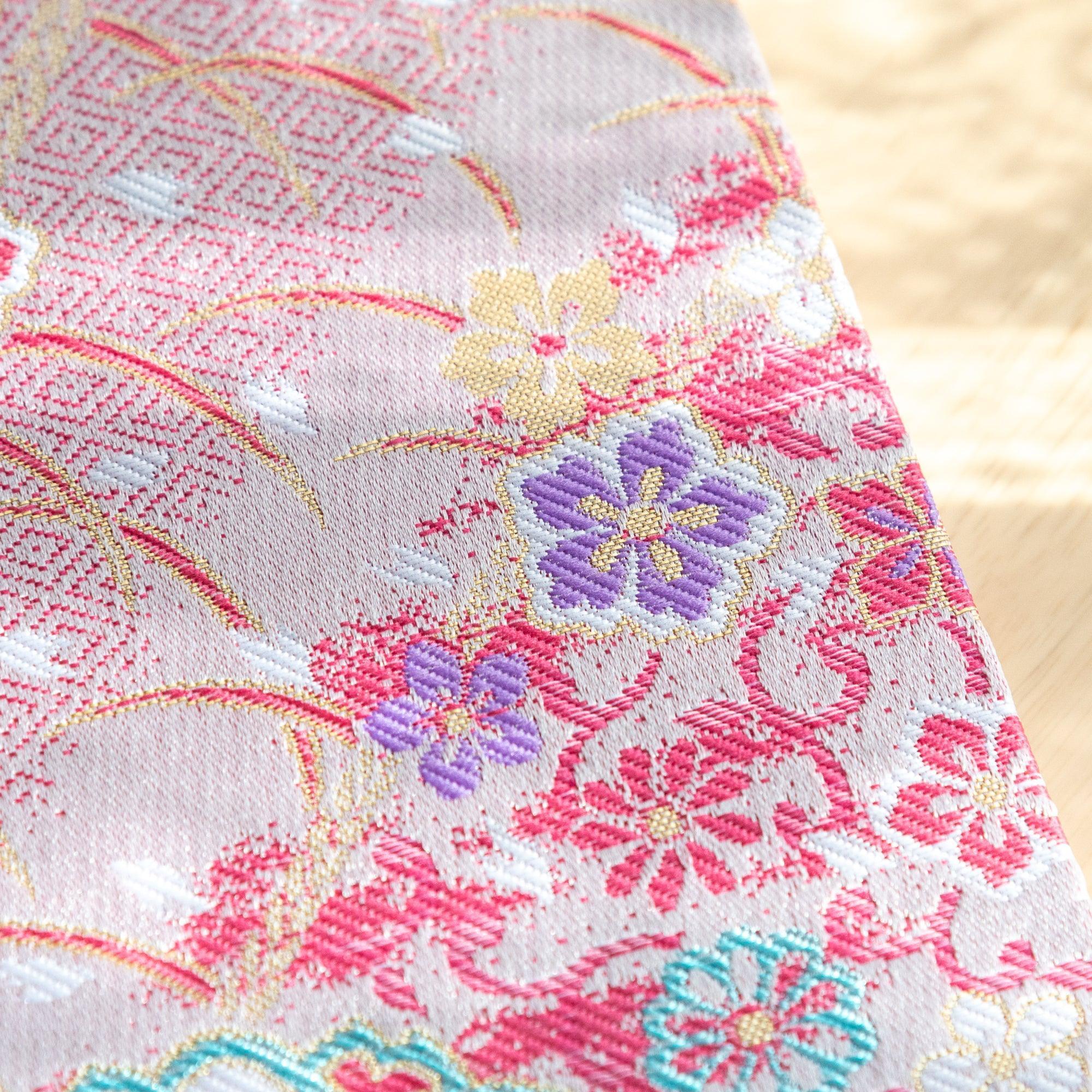 A Japanese notebook with a fabric cover featuring vibrant floral patterns in red, pink, and gold tones, placed on a wooden table.
