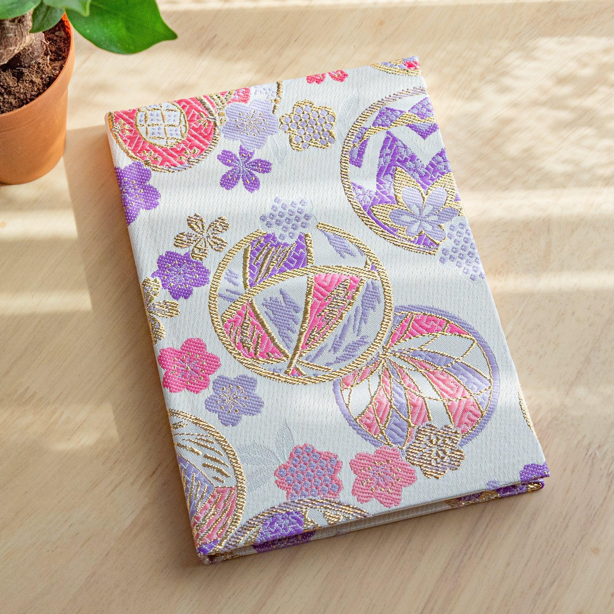 A Japanese notebook with an elegant fabric cover featuring traditional patterns of flowers and golden details, placed on a wooden table.