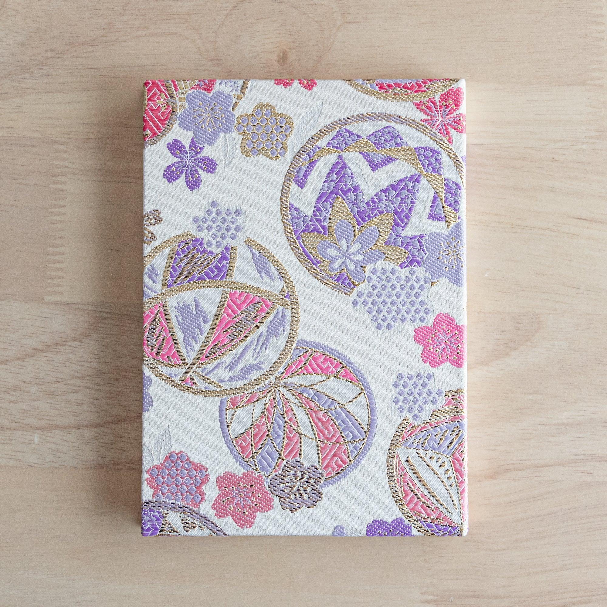 The back view of a Japanese notebook with a fabric cover decorated with pastel floral patterns and gold accents.