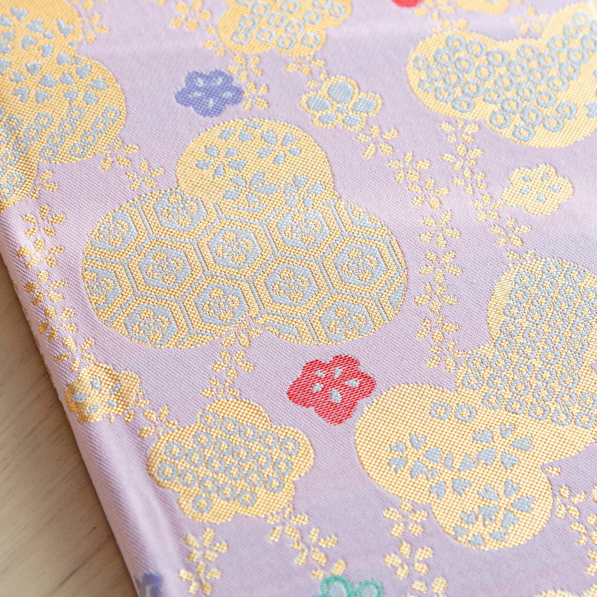 A close-up of the fabric cover of a Japanese notebook, highlighting intricate gold details and colorful floral patterns.