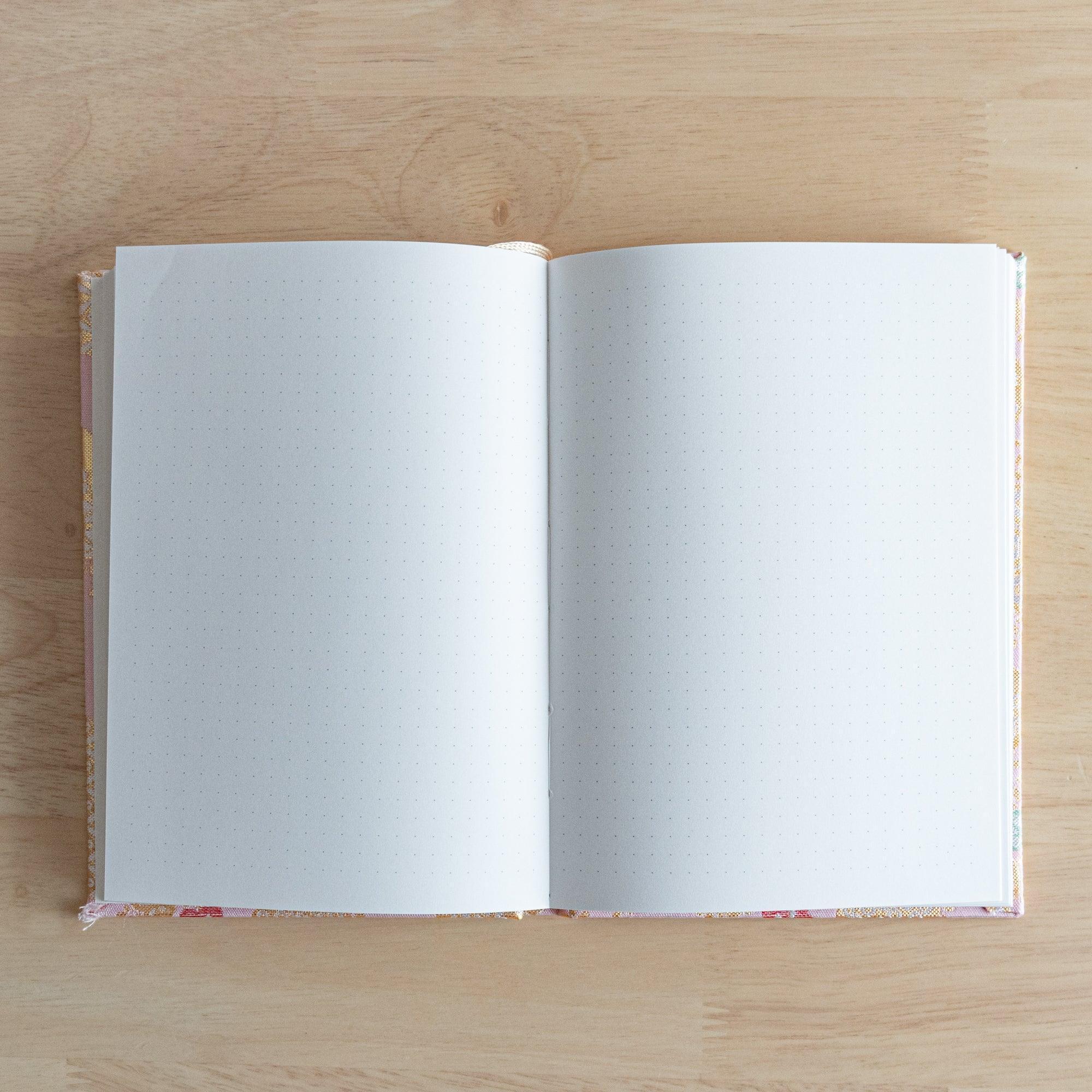 An open Japanese notebook showing white pages with a subtle dot grid pattern, ideal for writing or sketching.