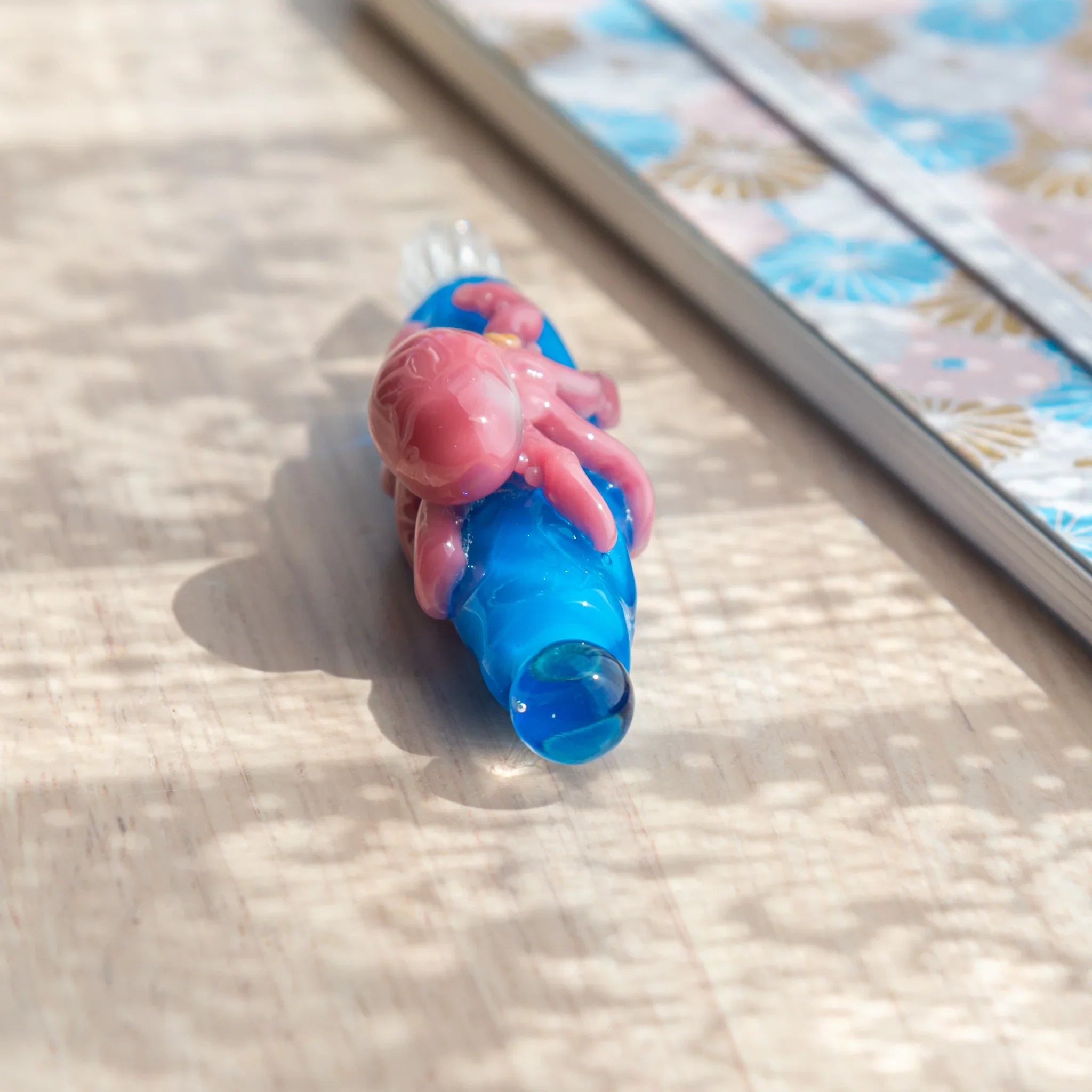 Close-up of blue glass Japanese dip pen from cap end showing pink octopus figurine with tentacles and blue ball cap