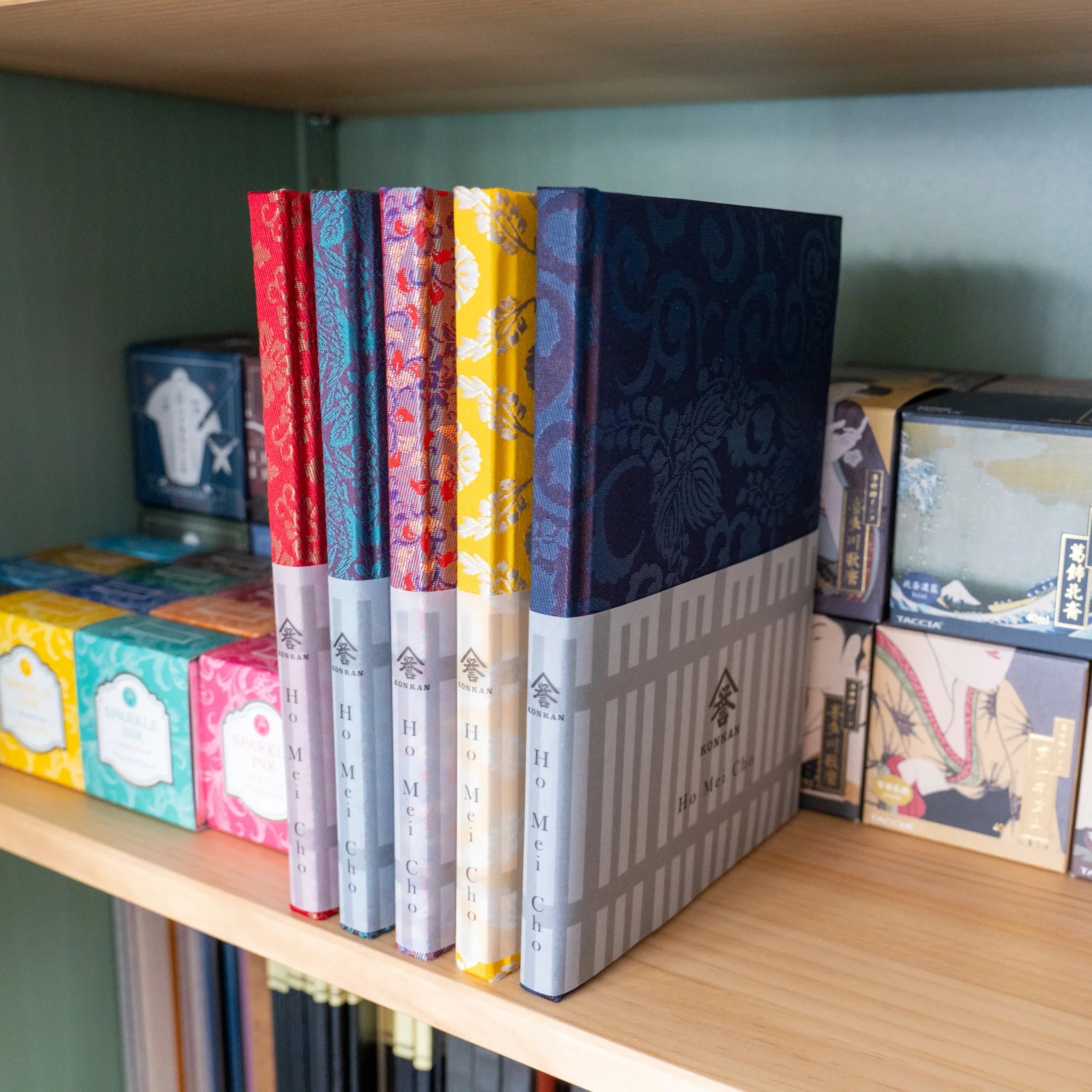 Oni Kiri Nishijin Homeicho notebook standing on wooden shelf with other colorway notebooks and Japanese gift products