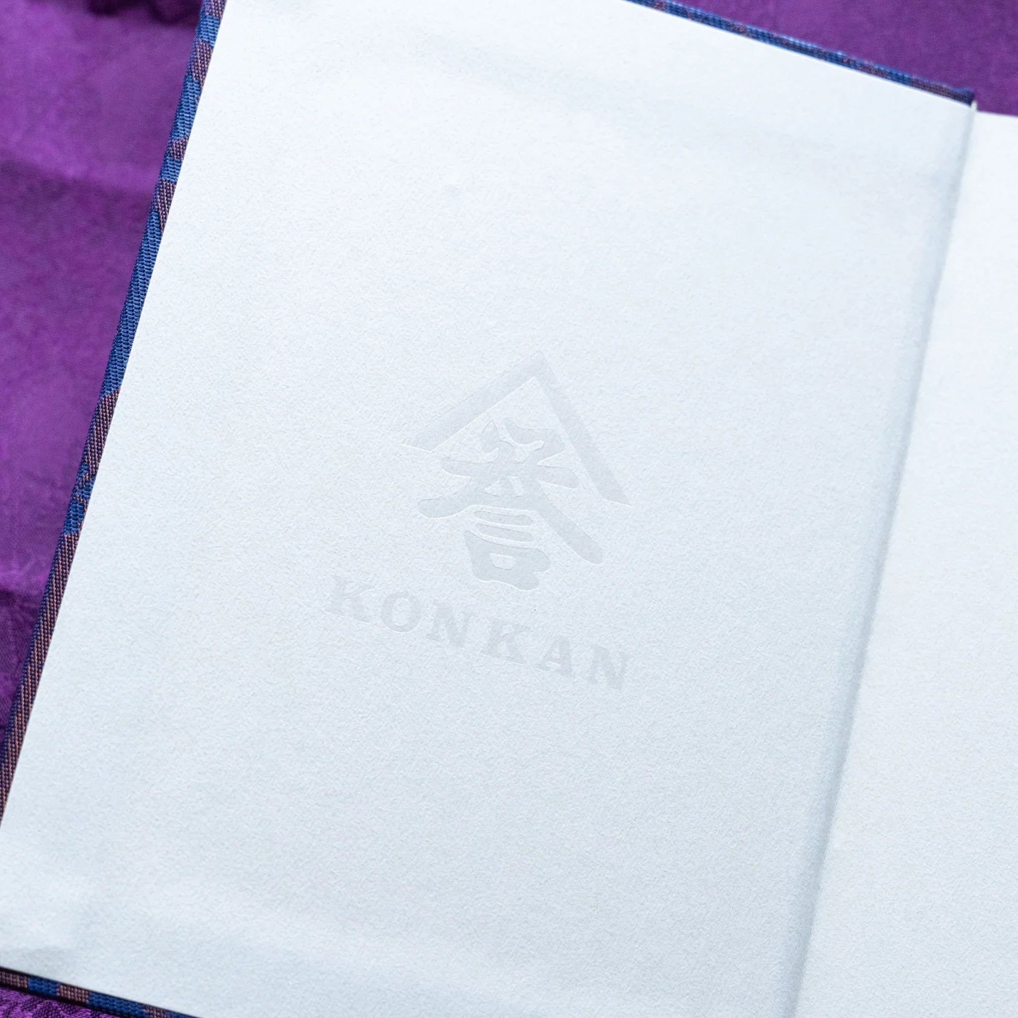 Oni Kiri Nishijin silk Homeicho notebook inner cover close-up showing KONKAN embossed logo on cream white endpaper
