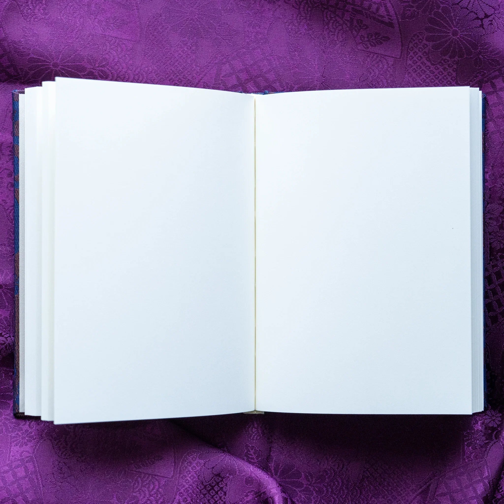 Oni Kiri Nishijin silk Homeicho notebook opened flat overhead showing blank white page spread with blue cover edges on purple