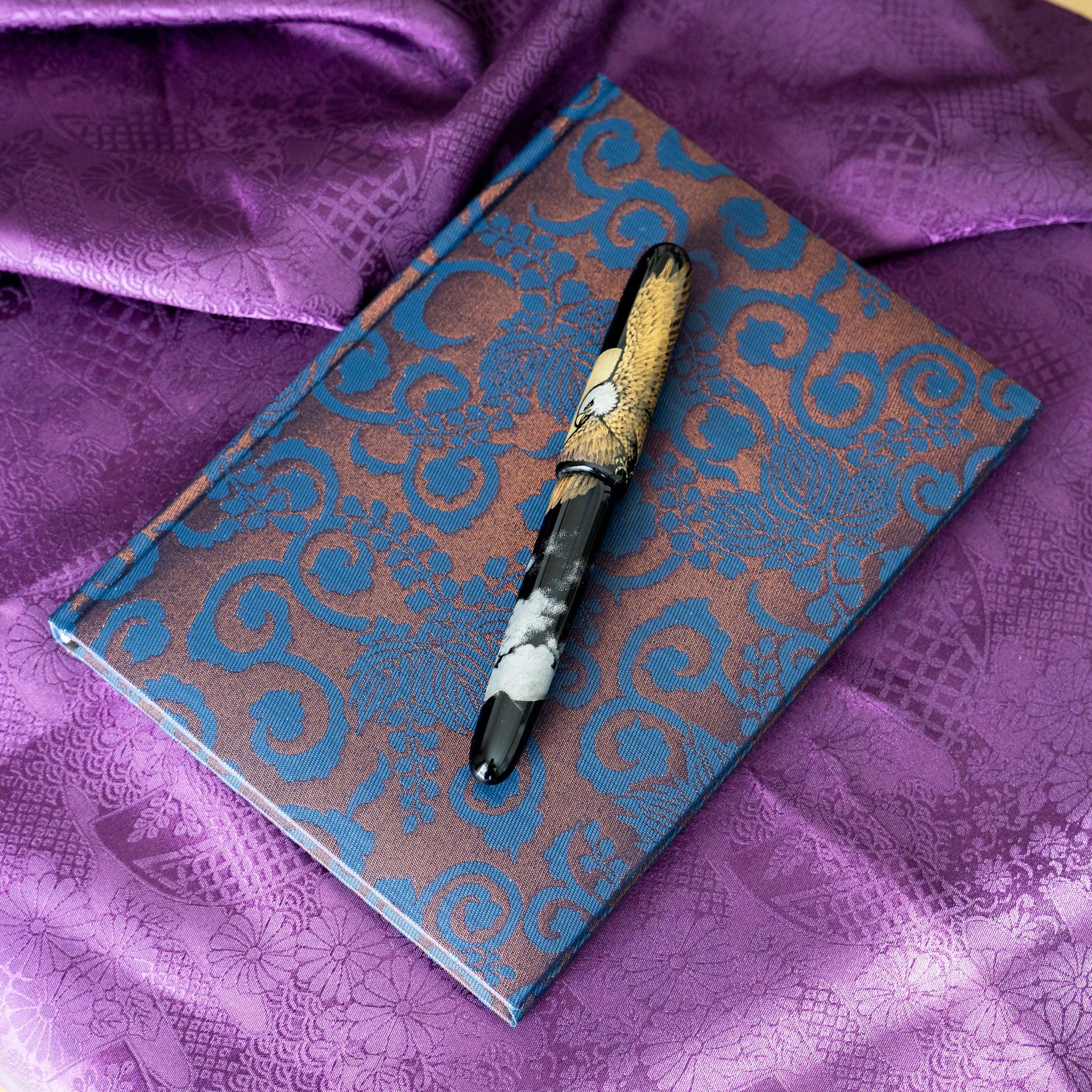 Oni Kiri Nishijin silk Homeicho notebook on purple fabric with maki-e decorated fountain pen placed diagonally across cover