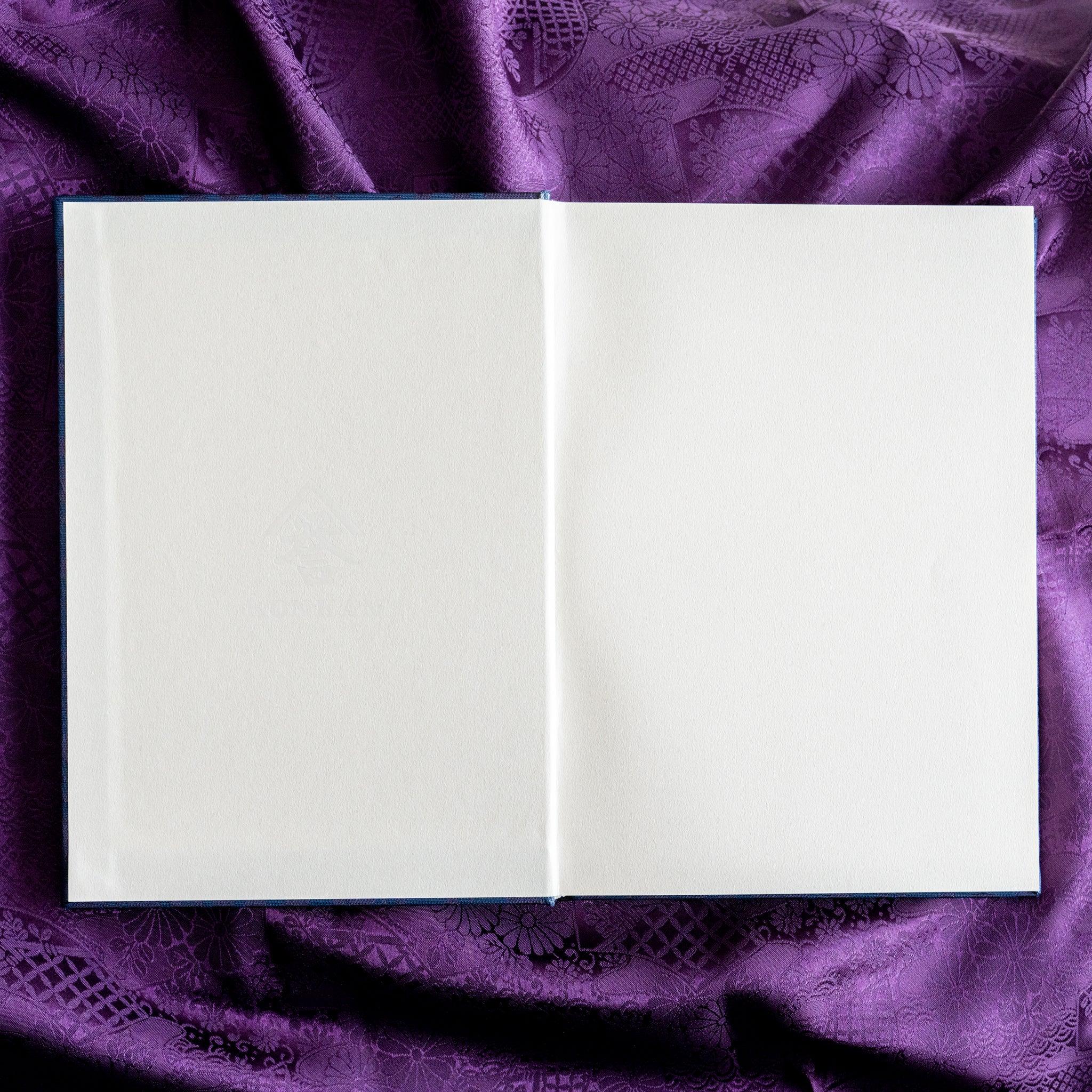 Oni Kiri Nishijin silk Homeicho notebook opened flat overhead showing blank white page spread on purple fabric background