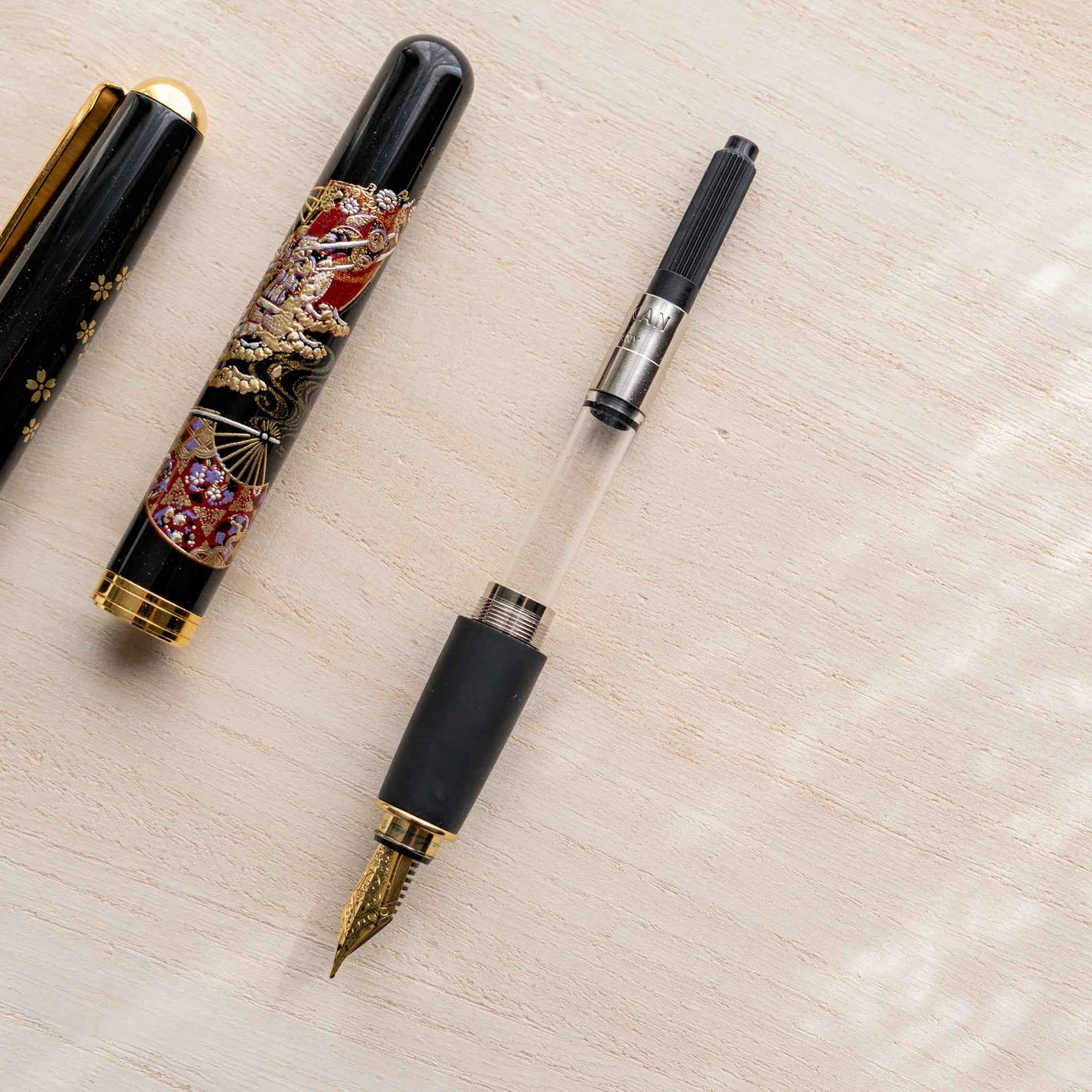 Disassembled Yamanaka Japanese fountain pen showing barrel, nib section, and Pelikan piston converter.