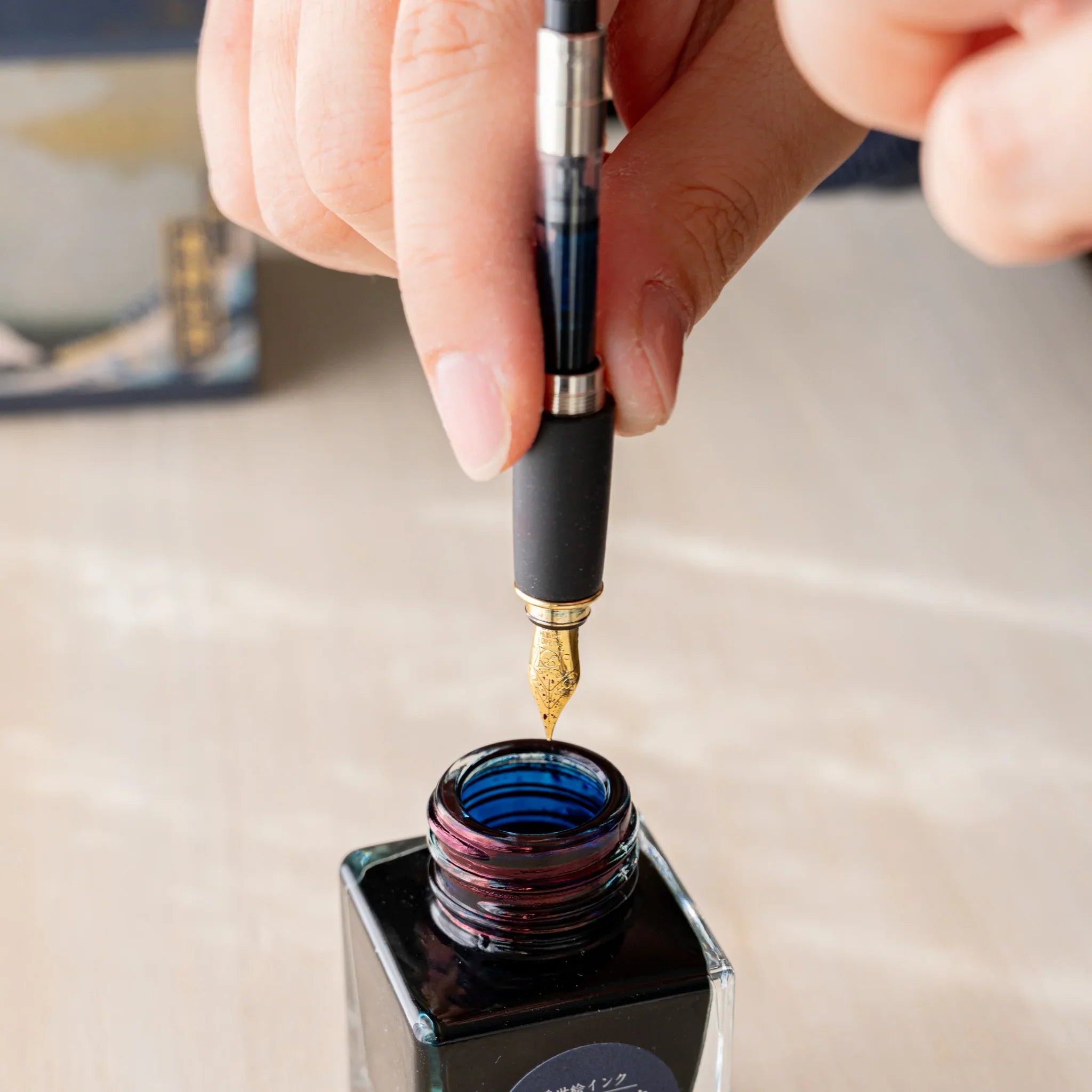 Hand holding a Yamanaka Japanese fountain pen with Pelikan converter installed, dipping nib into ink.