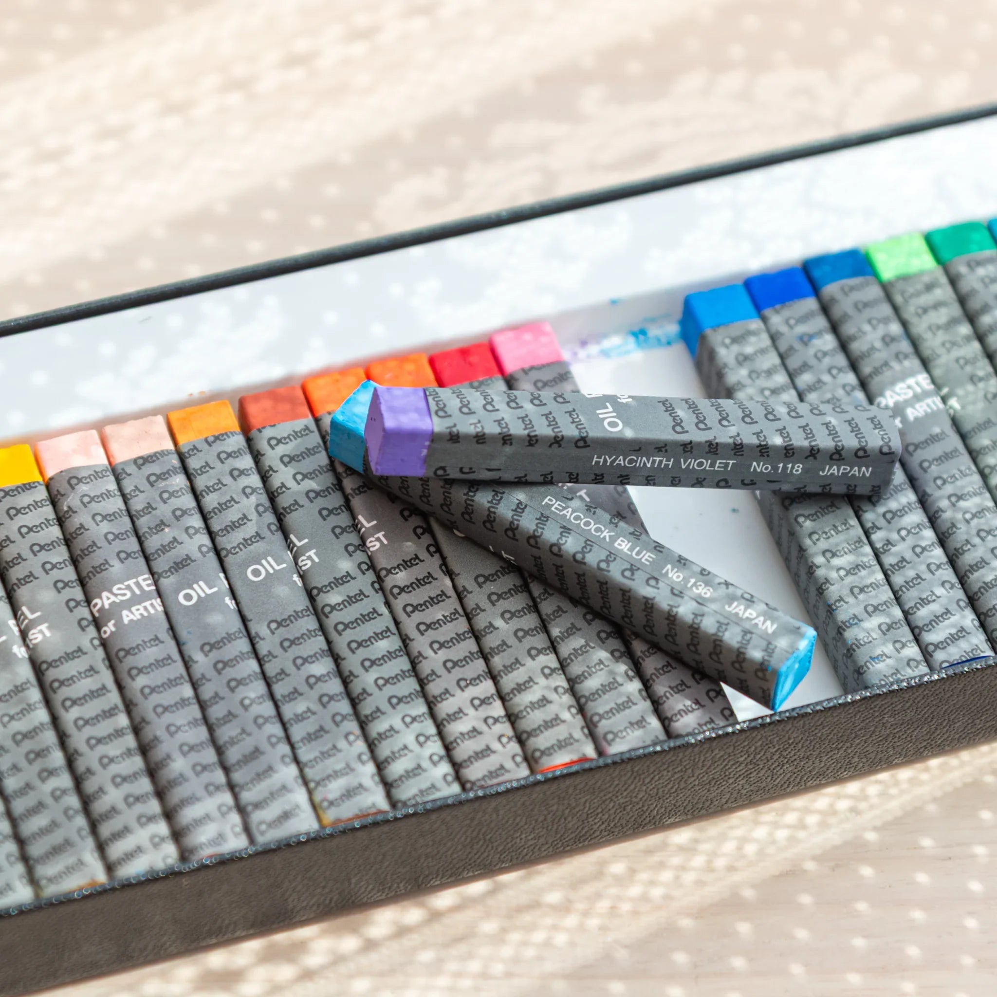 Hyacinth violet and peacock blue Pentel Japanese Oil Pastels rest diagonally for arts and crafts.