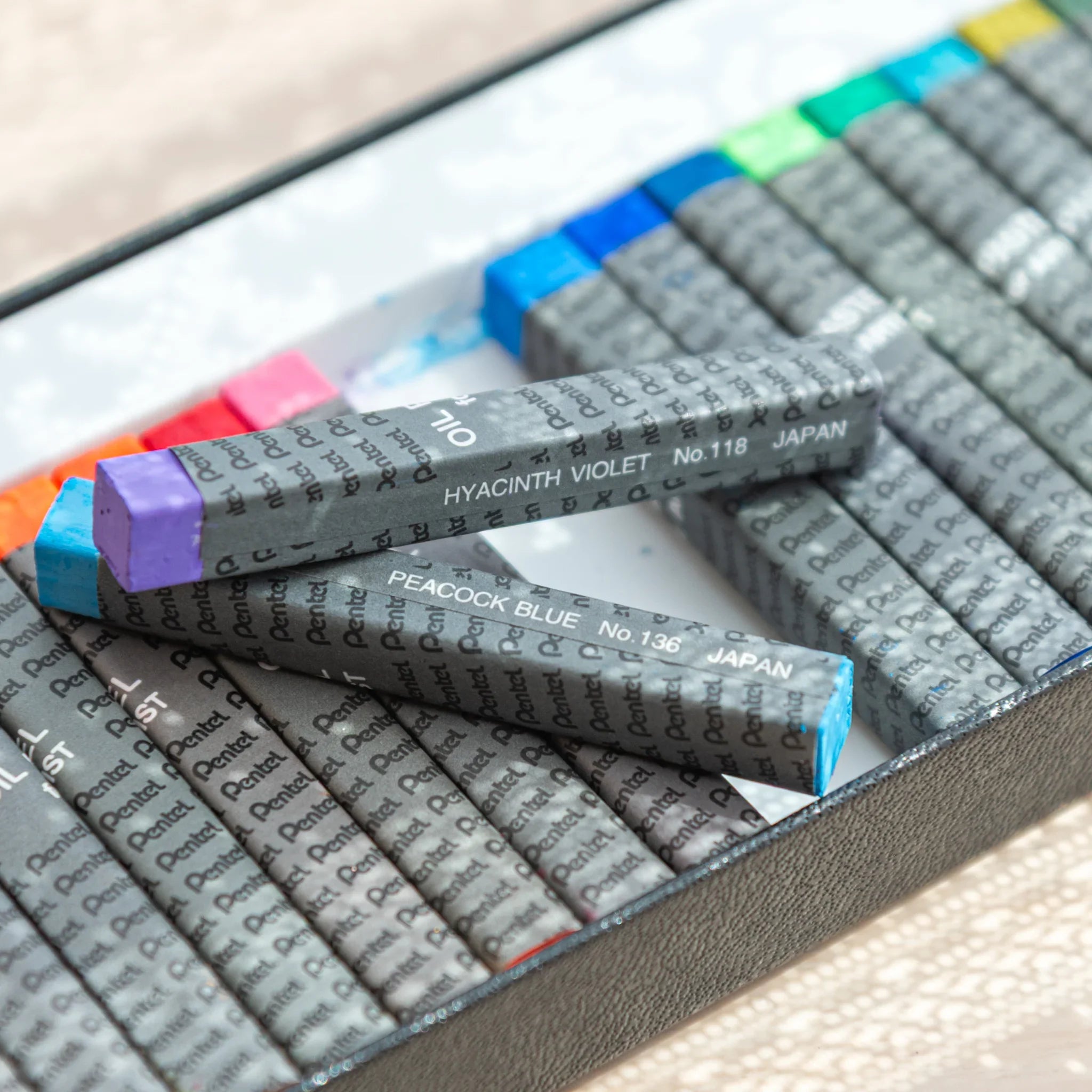 Close-up of two Pentel Japanese Oil Pastels in peacock blue and violet, highlighting arts and crafts colors.