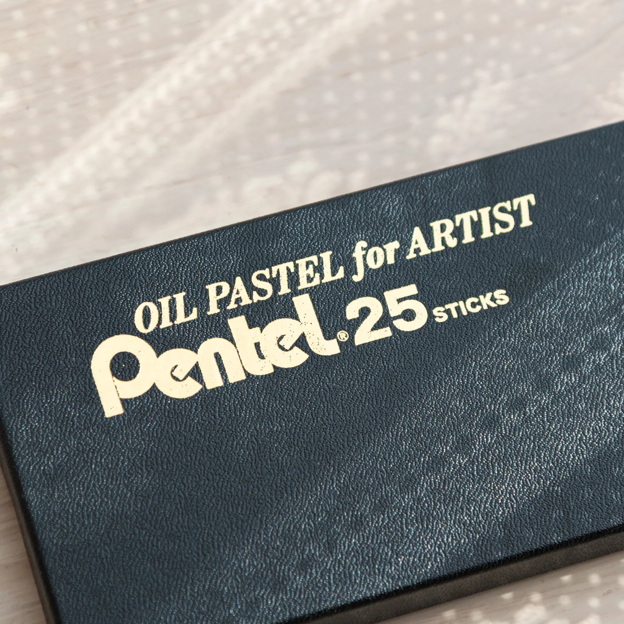 Close-up of dark green Pentel Oil Pastel for Artist 25-stick box lid with embossed text on textured surface