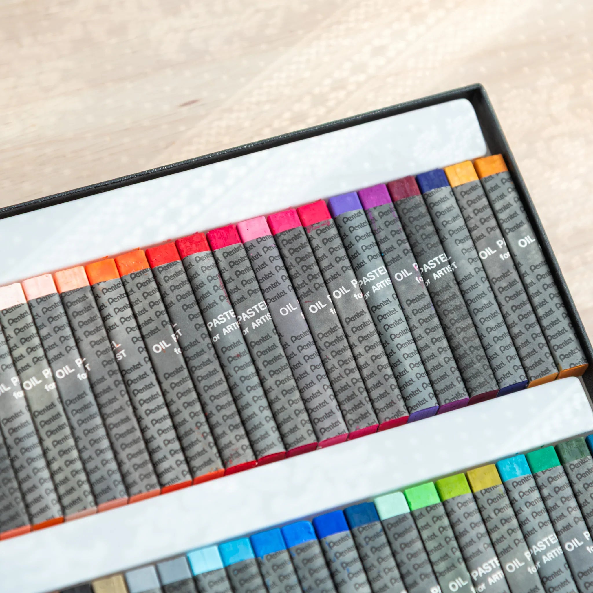 Angled view of Pentel oil pastel box from opposite end showing warm-cool color transition across 49 sticks in two trays