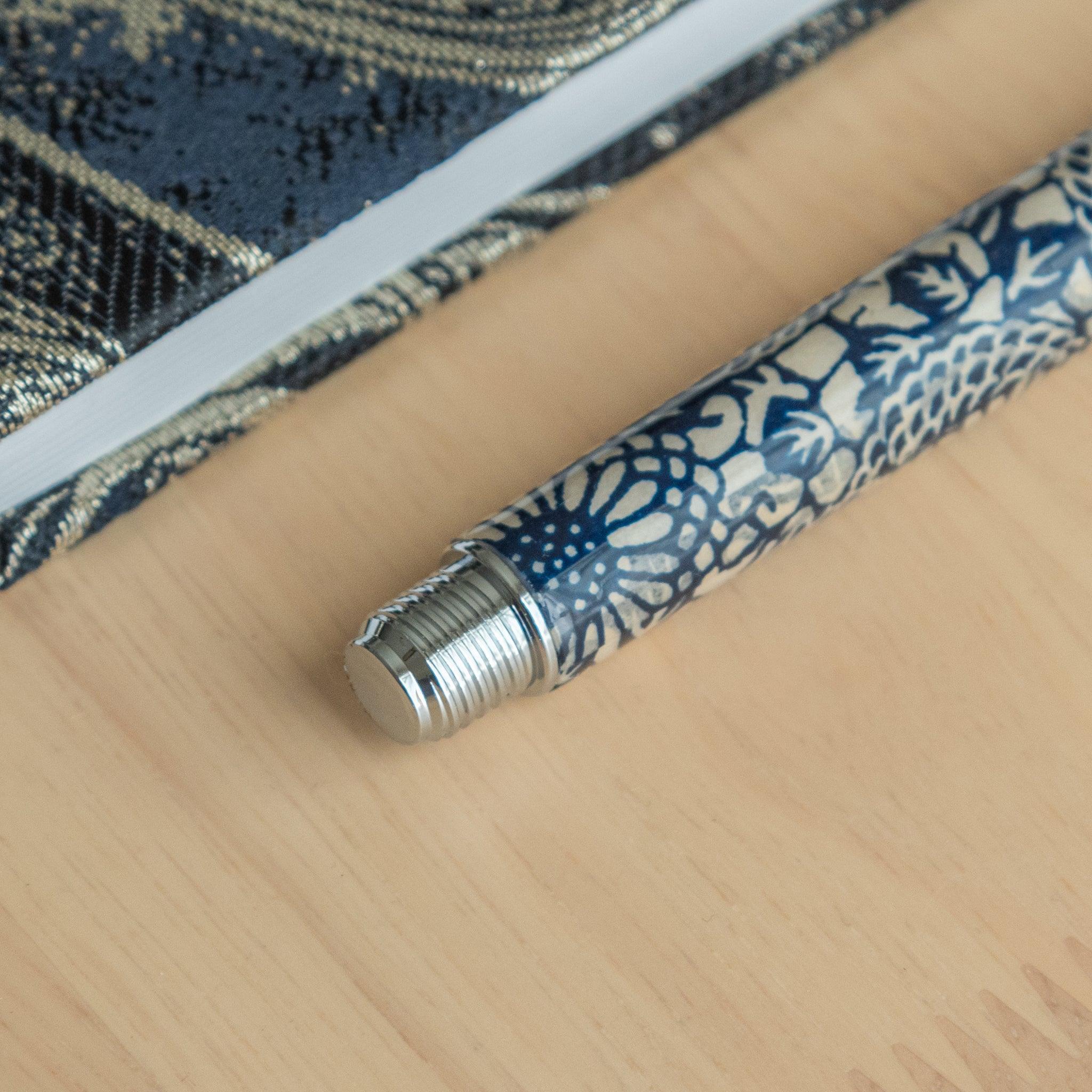 Close-up of the threaded end of a Japanese stationery fountain pen with blue chrysanthemum patterns, placed on a wooden surface.