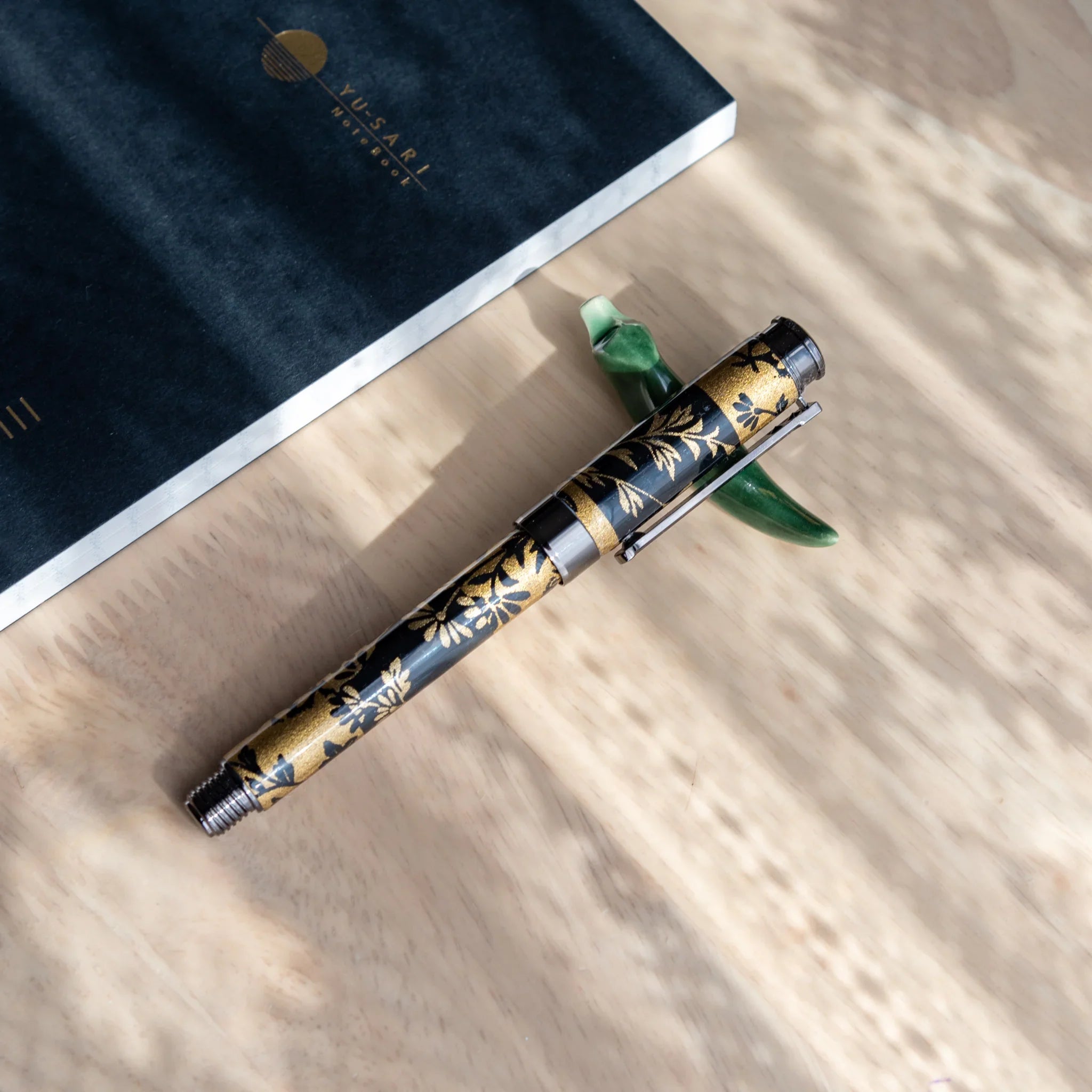 Full-length dark fountain pen with black and gold autumn grass pattern design on cream-colored display surface