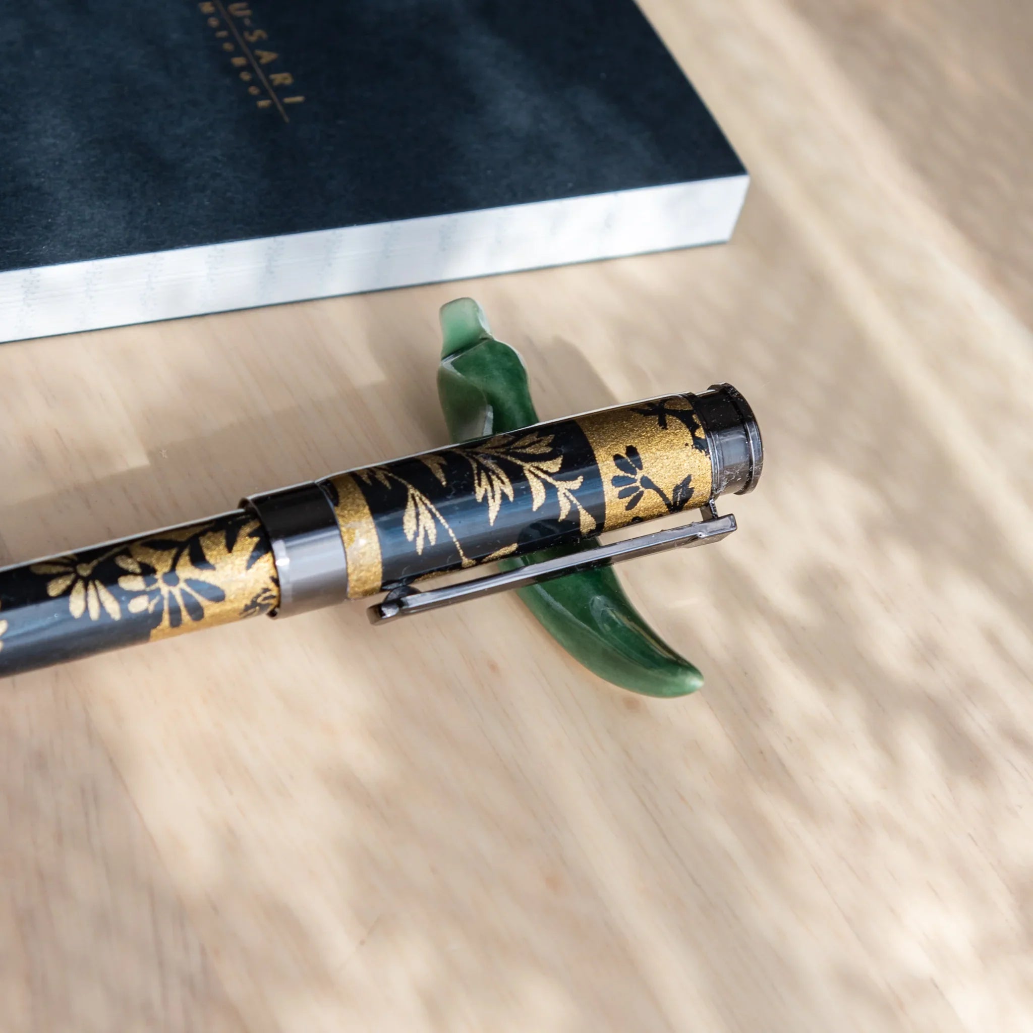 Flat lay arrangement of multiple ceramic pepper pen rests in varied earth tone colors on wooden writing surface