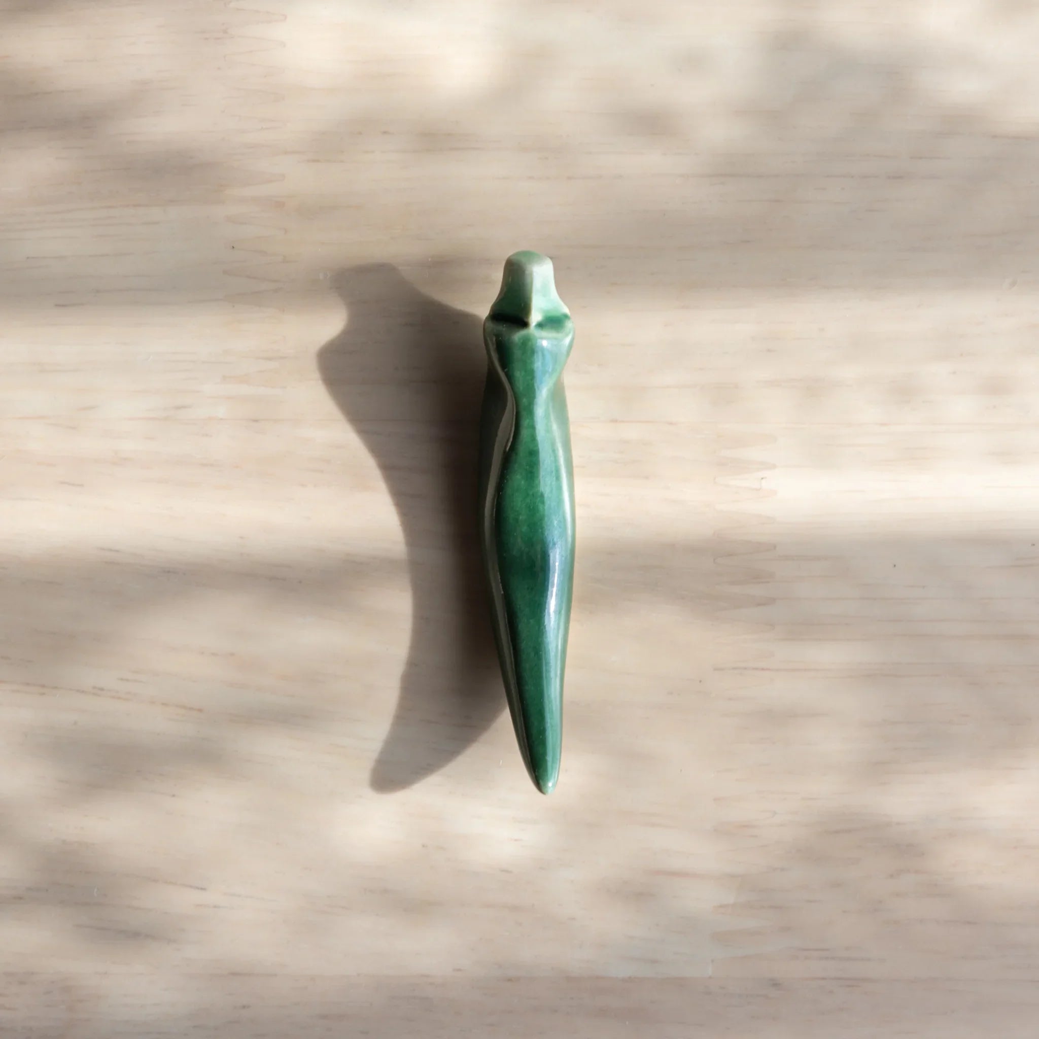 Single green pepper-shaped handcrafted ceramic pen rest displayed upright with elongated stem on wooden surface