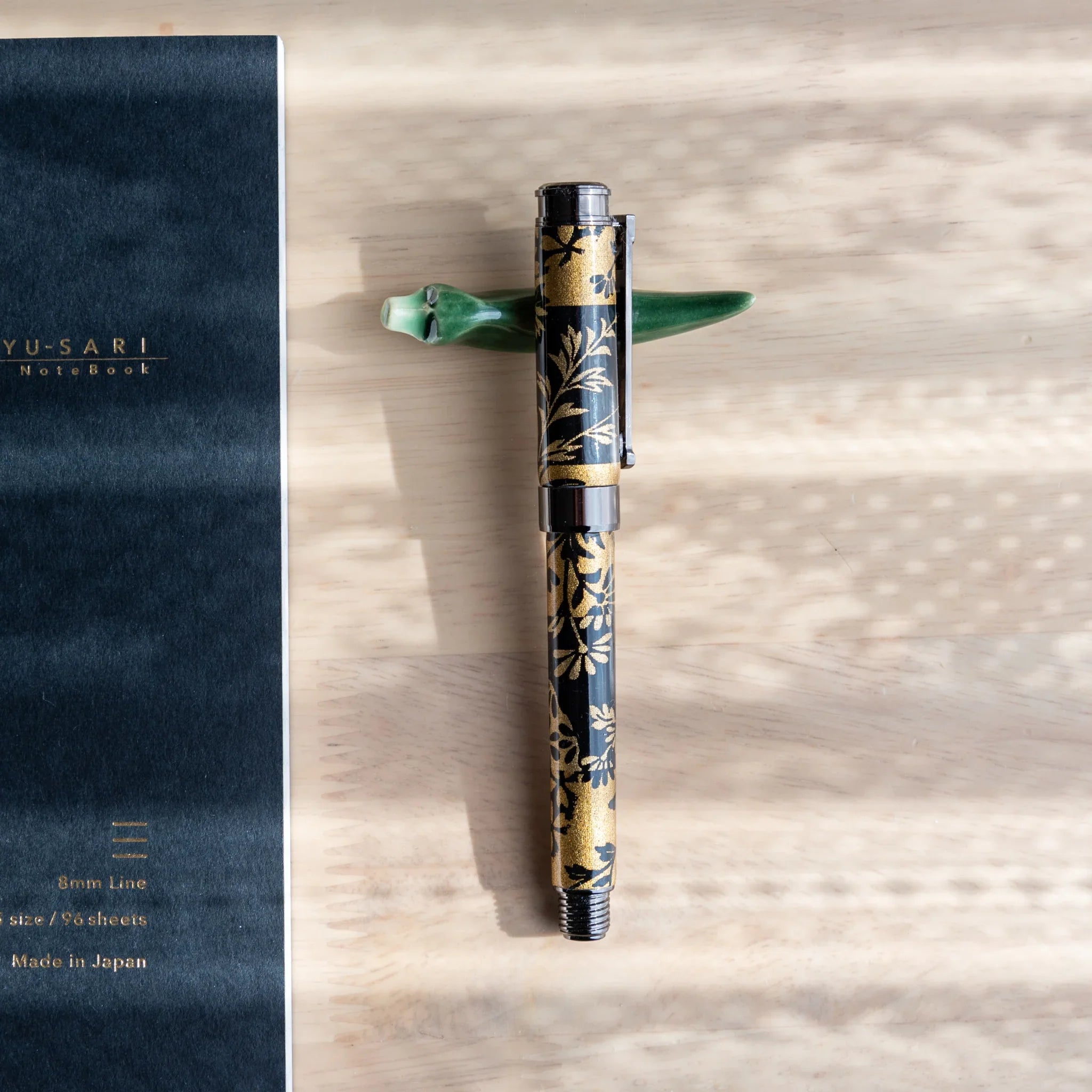 Dark navy fountain pen featuring gold and floral design elements resting on botanical Mino washi wrapper background