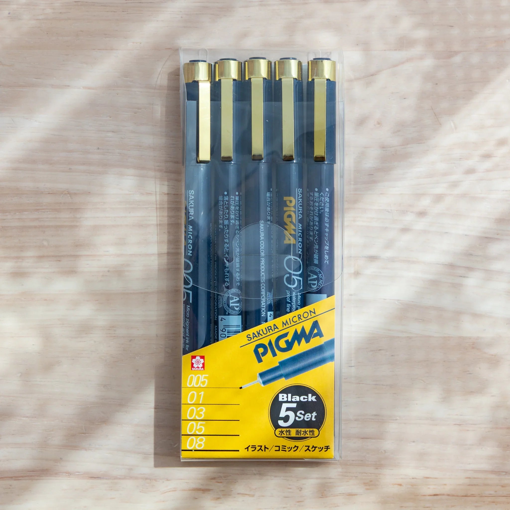 pigma micron pens set of five fineliner pens with assorted tip sizes in clear plastic packaging on wooden desk
