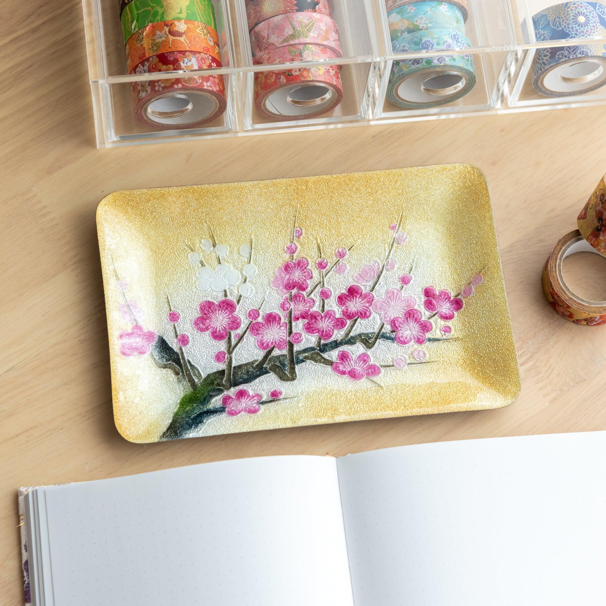 Japanese shippo ware pen tray with pink and white plum blossom design on gold enamel, on wood desk with washi tape organizer
